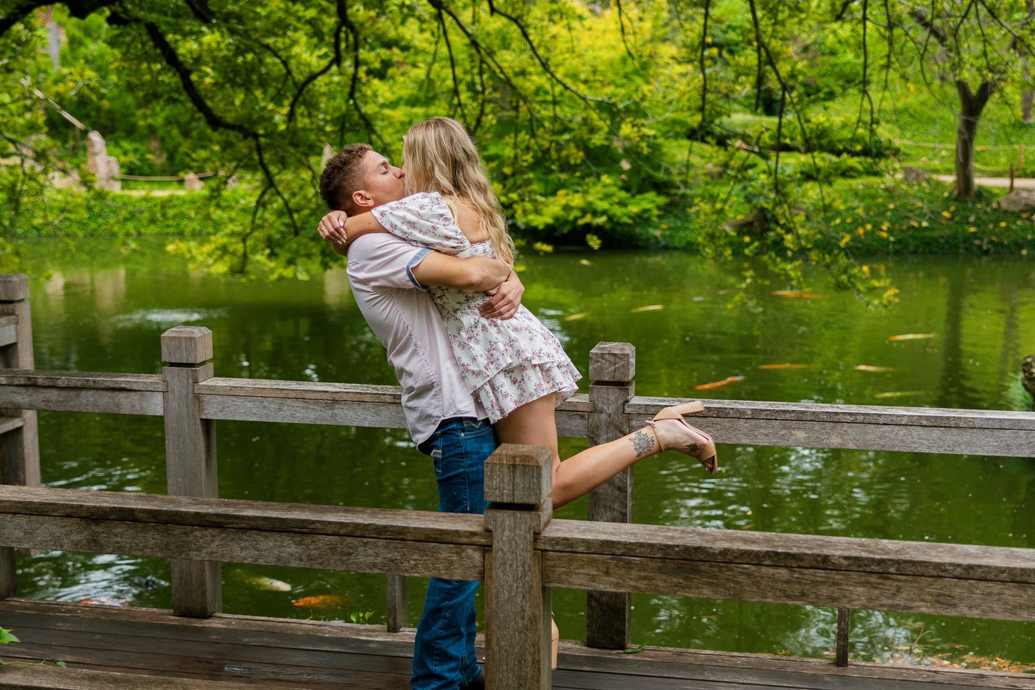 A family enjoys a peaceful moment feeding ducks at a scenic pond surrounded by lush green trees and wooden railings.