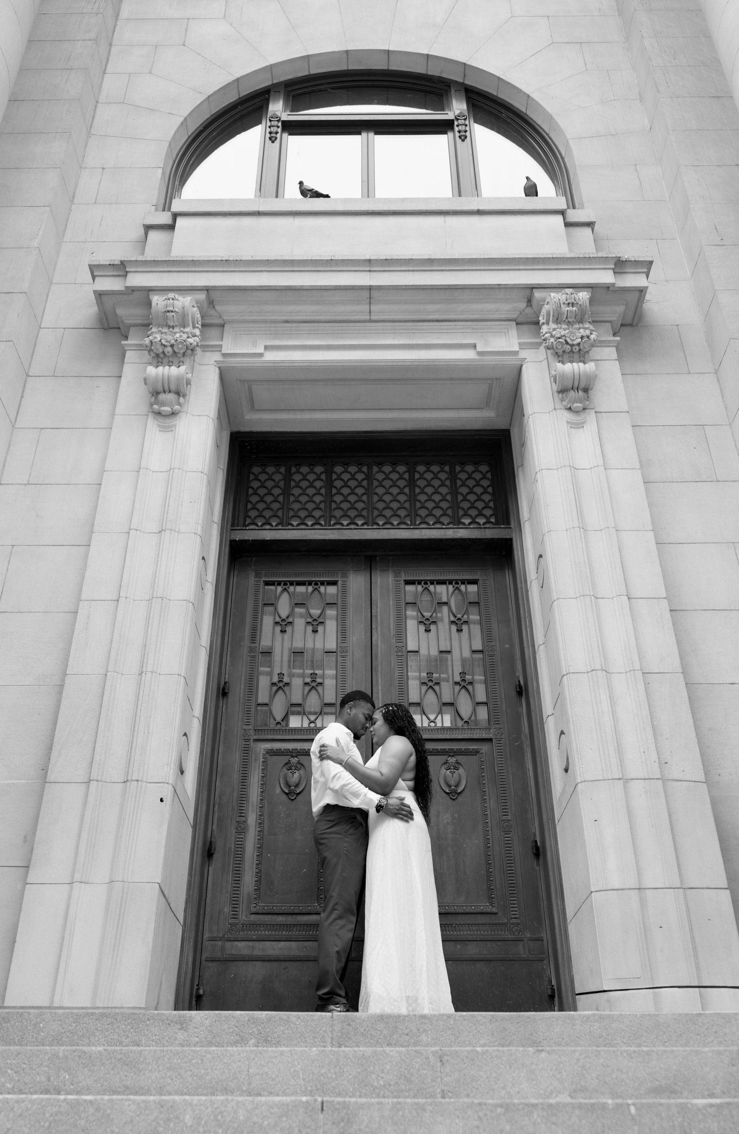 A classic black and white wedding portrait in front of an ornate stone archway.