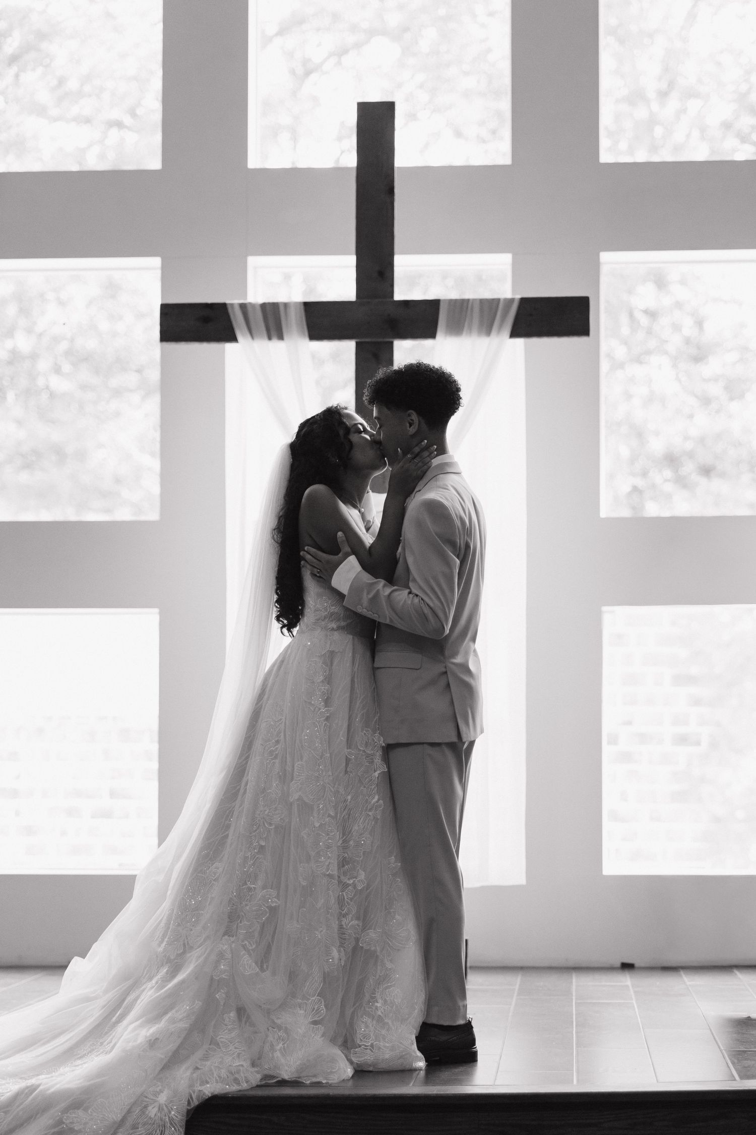Black and white wedding photo showing silhouettes of a couple embracing against a bright window backdrop.