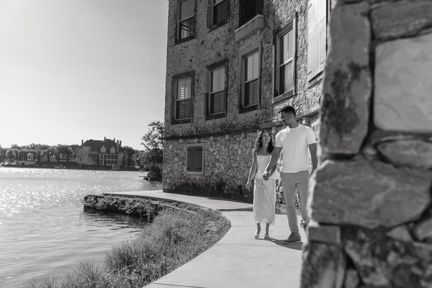 A couple walks along a stone building wall in dramatic black and white photography.