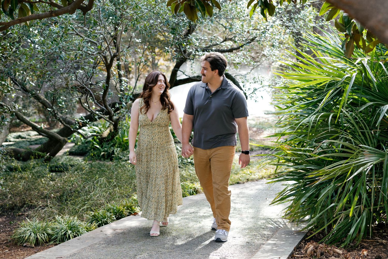 Couple holding hands walking on a garden path surrounded by lush tropical greenery and palm trees.