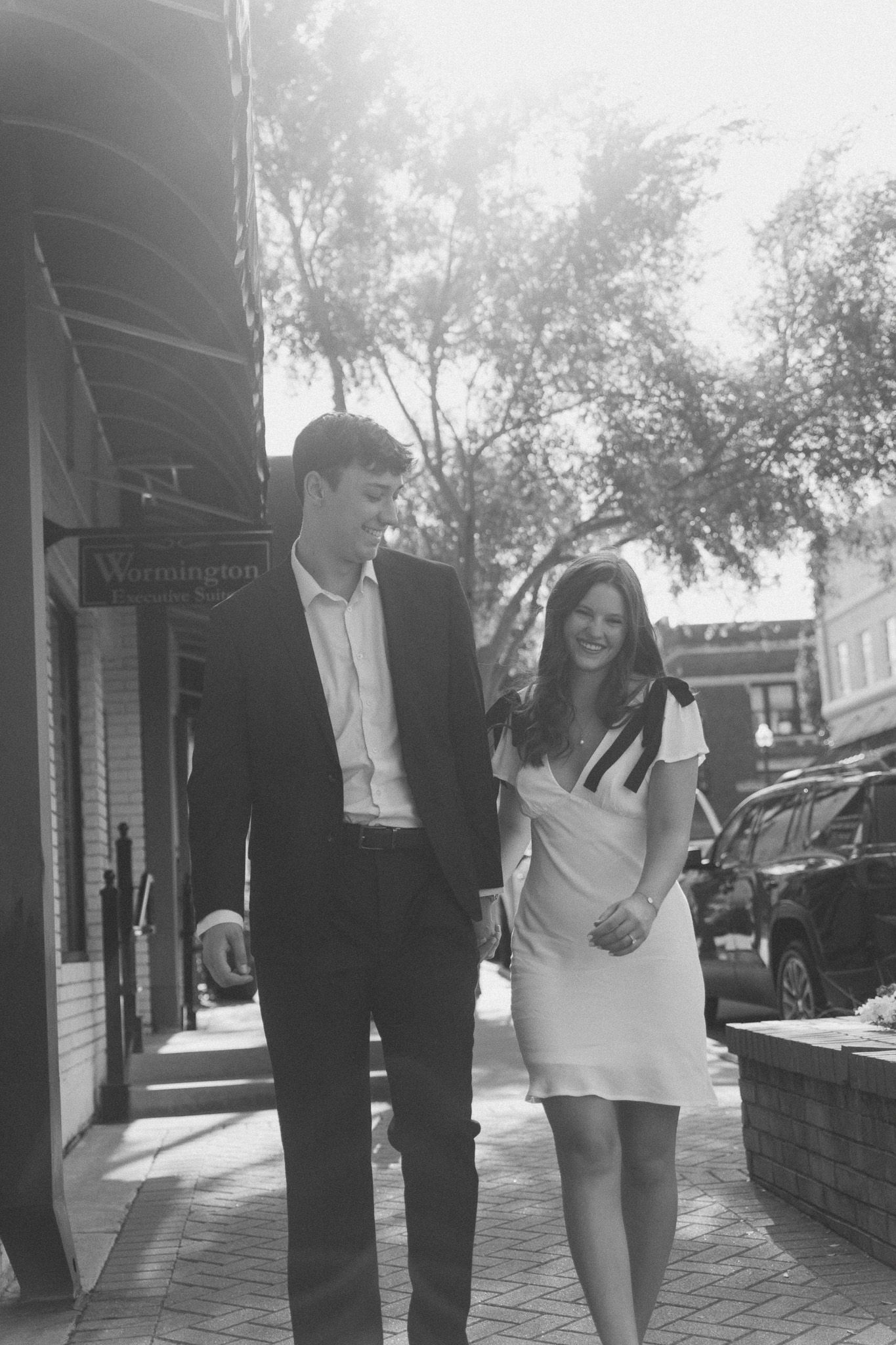Black and white photo series of a couple walking and laughing together on a brick sidewalk.