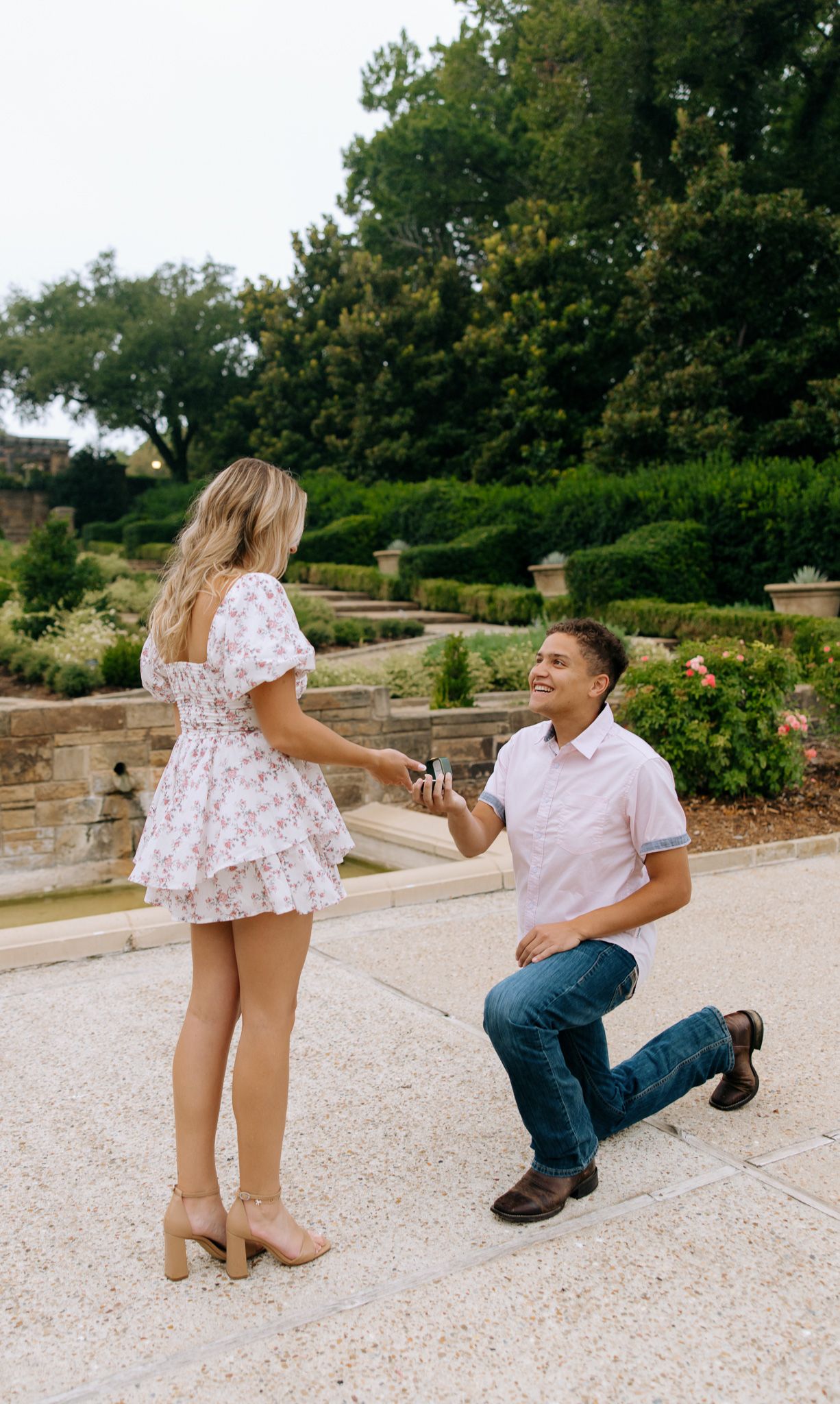 A couple shares a playful moment in a garden setting as they pose for a series of candid photos on stone steps.