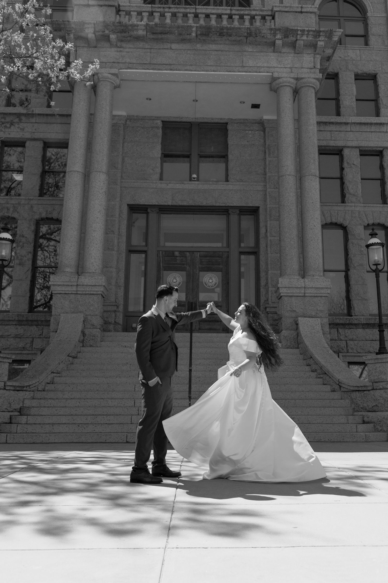 Black and white photo of a couple dancing in wedding attire on steps of a historic stone building.