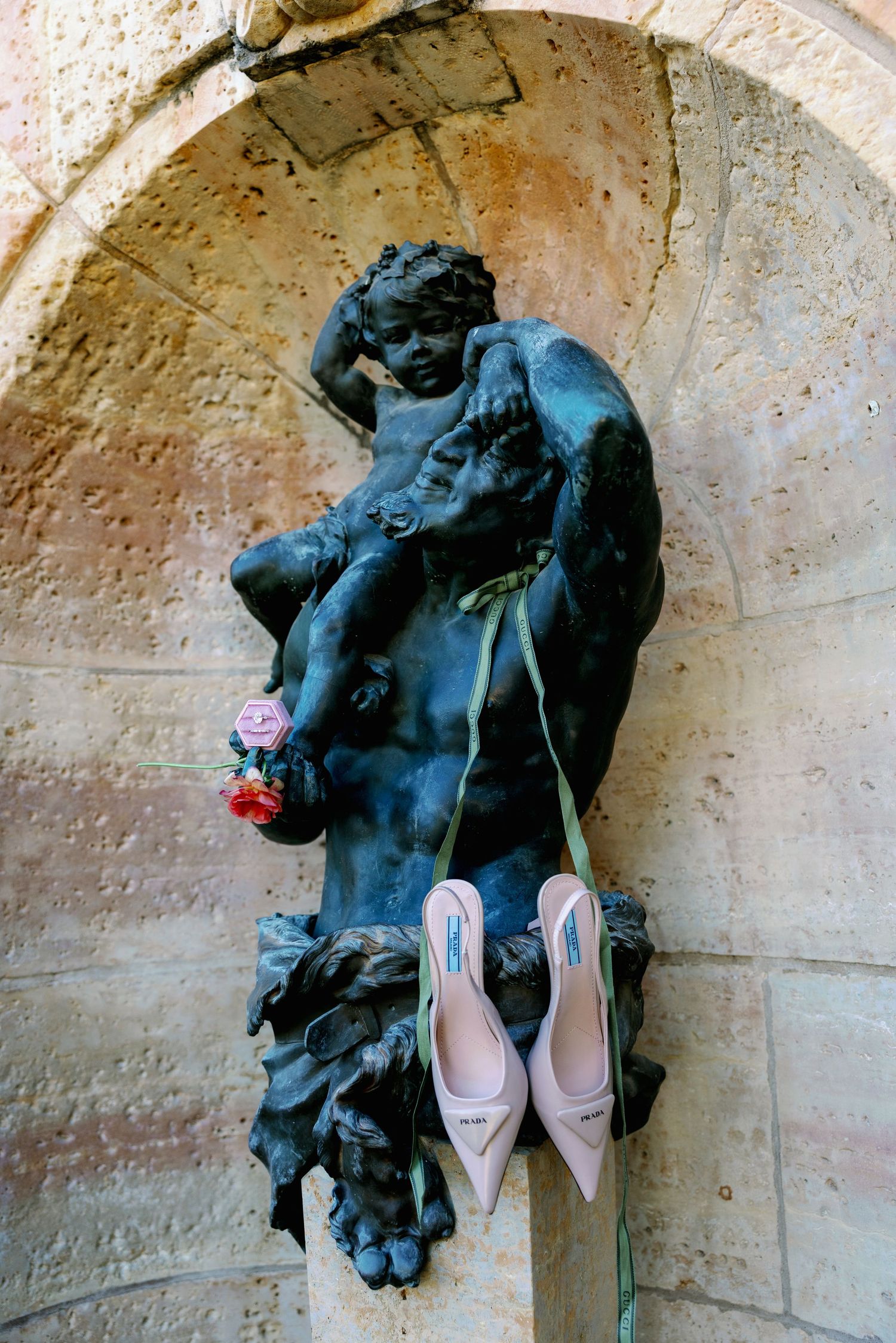 Bronze cherub statue in stone alcove with pink bridal heels and rose, elegant wedding detail photography.