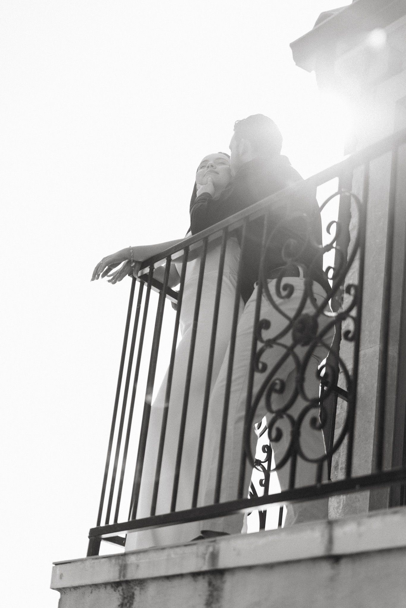 Silhouettes against bright sunlight on an ornate metal balcony railing.