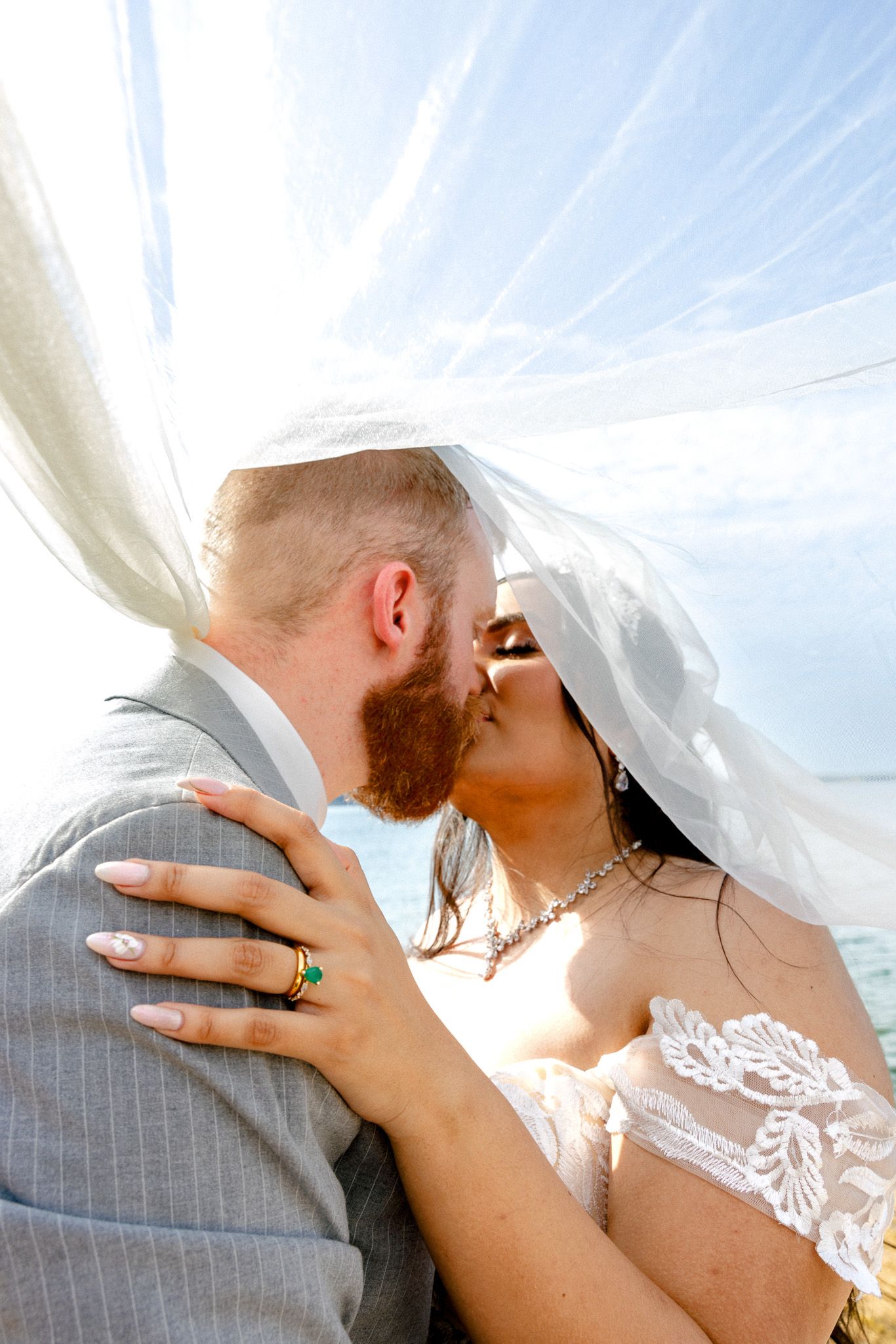 Romantic moment under flowing white veil with sunlight streaming through.