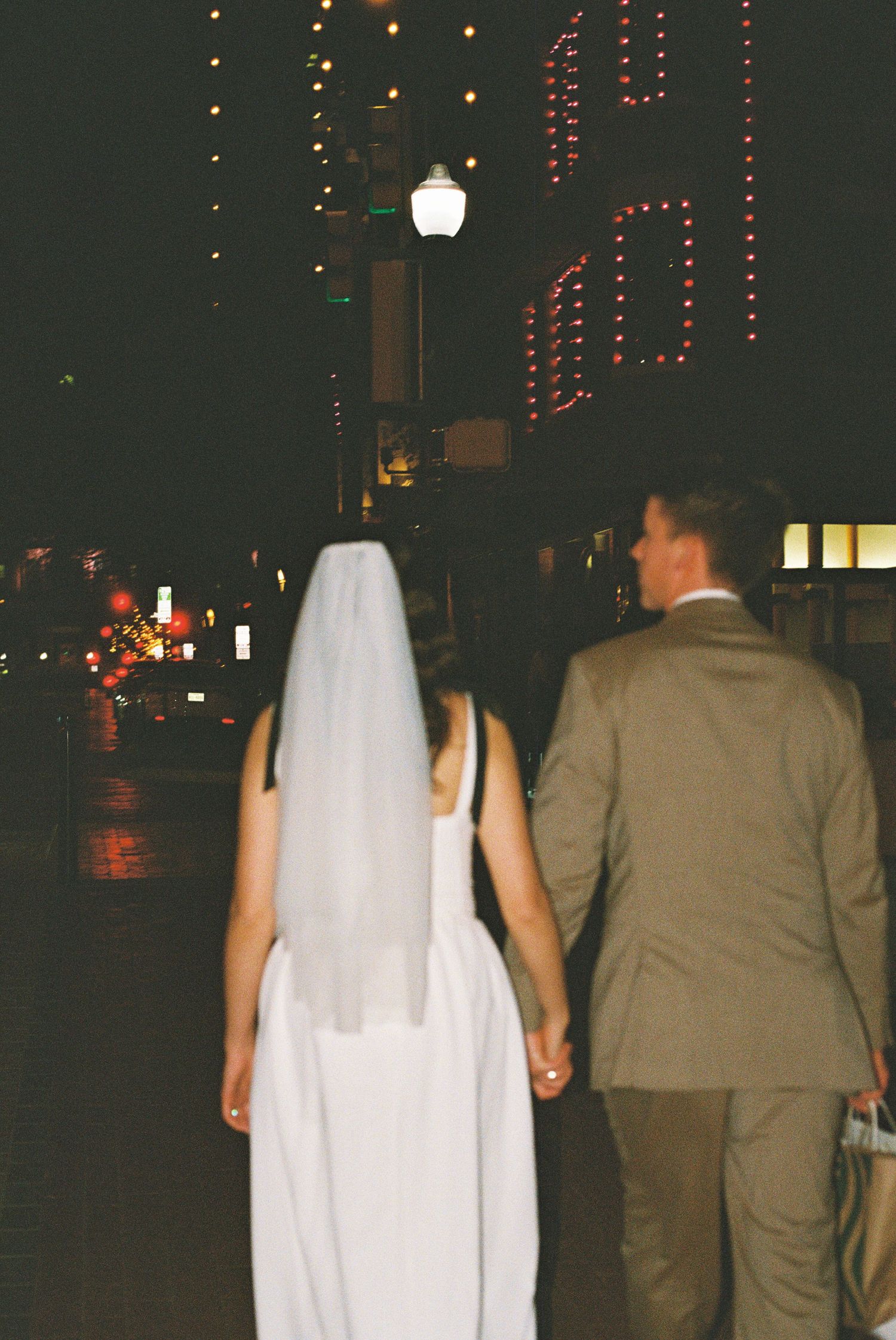 Bride and groom walking hand in hand at night on a city street, bride wearing a veil.