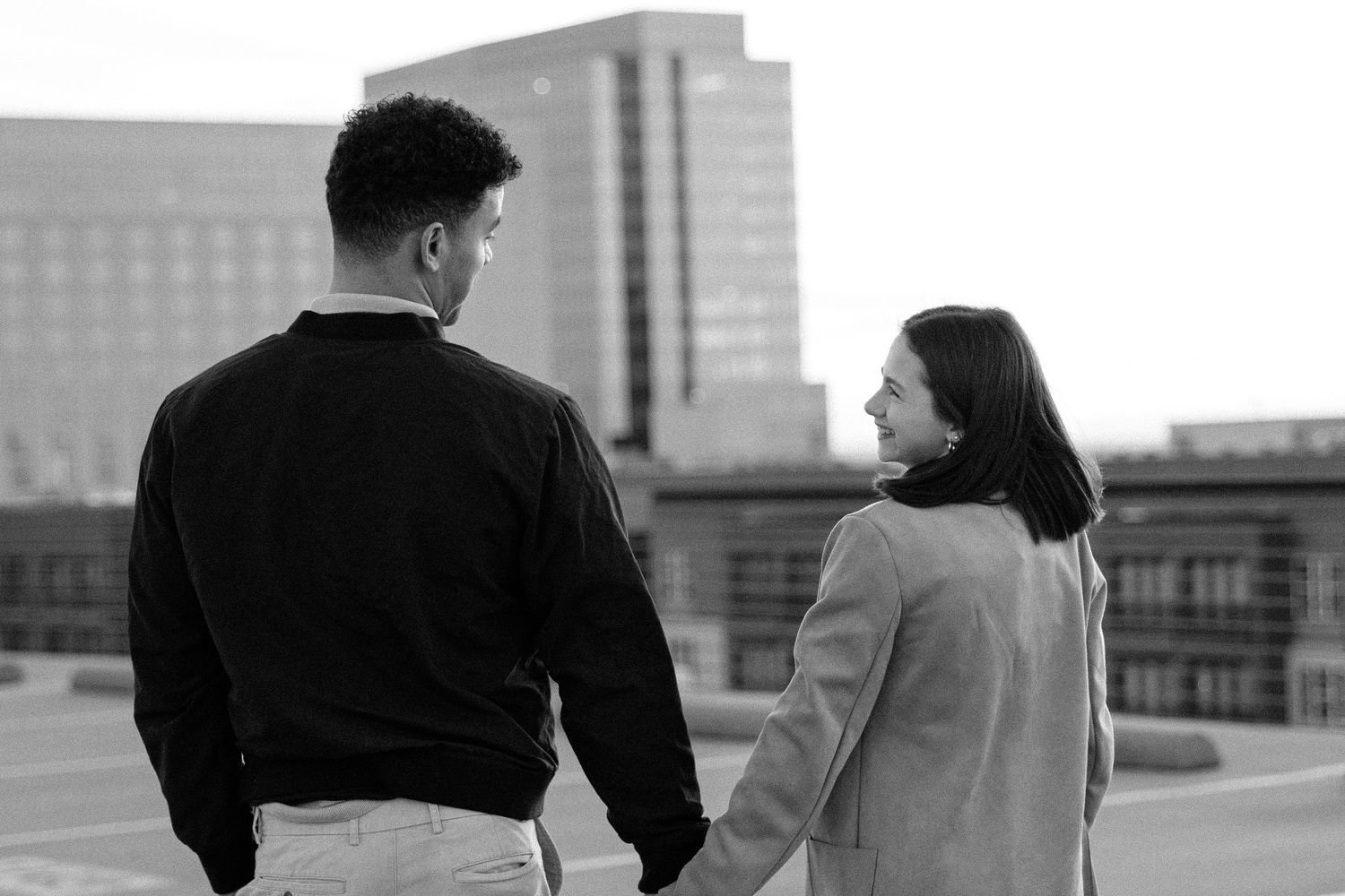 Black and white photo of a couple holding hands, looking at each other with a city skyline in the background.