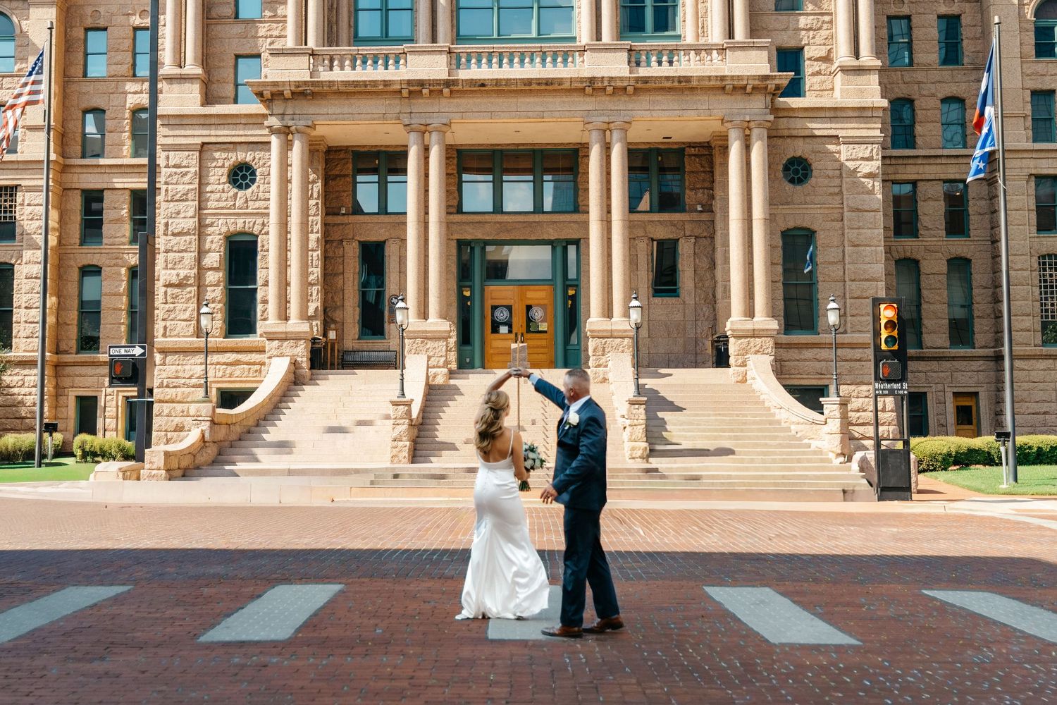 Couple in formal wedding attire standing on the steps of a grand historic stone building with columns.