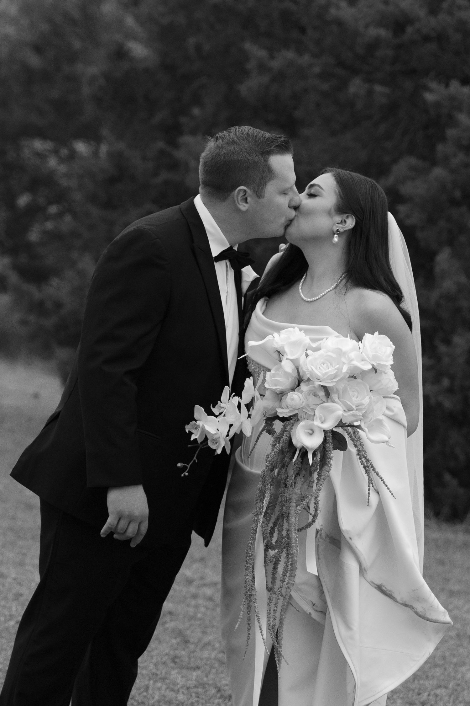 A romantic black and white wedding photo series showing a couple sharing intimate kisses while holding a bouquet of white roses.