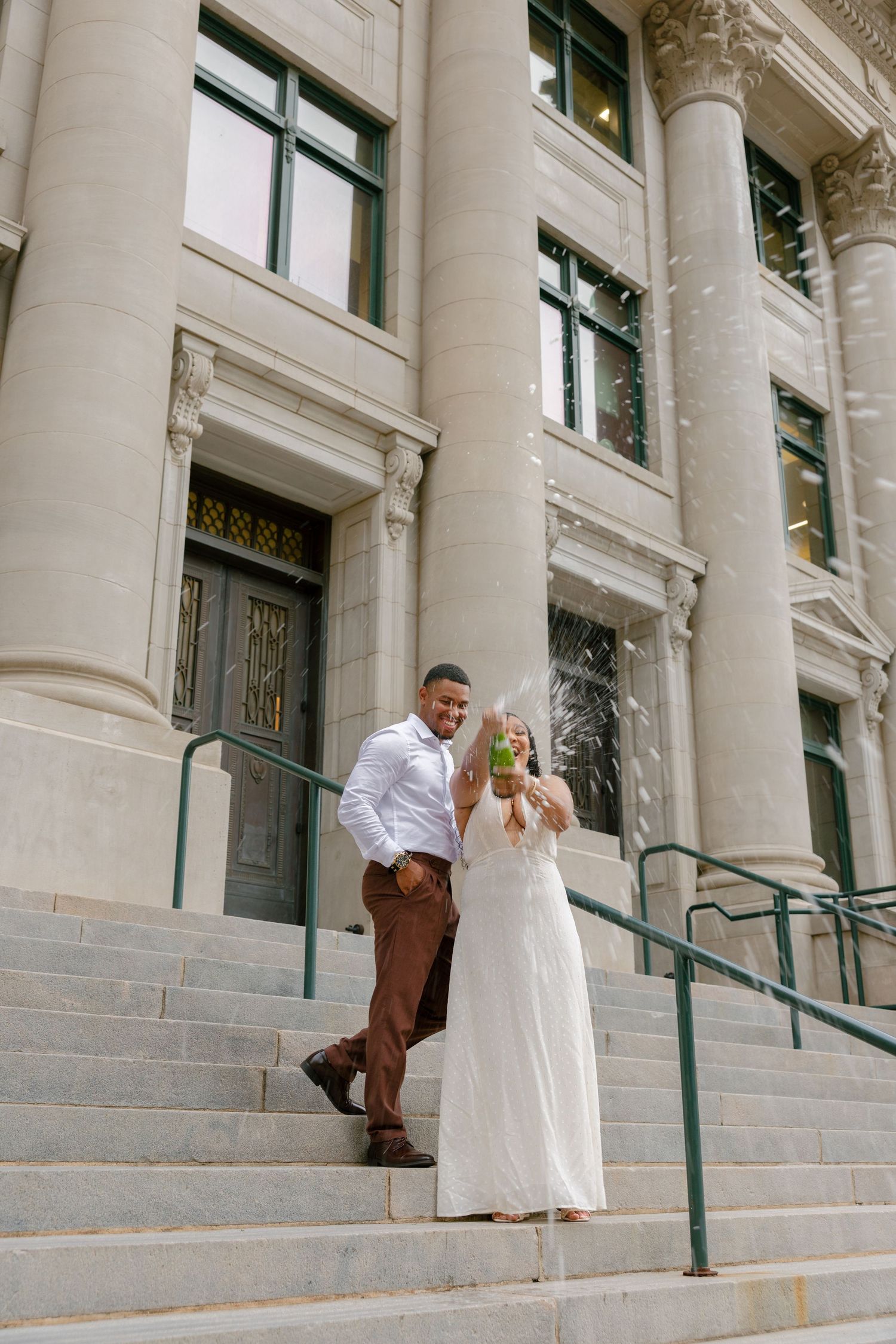 A couple stands on the steps of a grand historic building with white columns and ornate architectural details.
