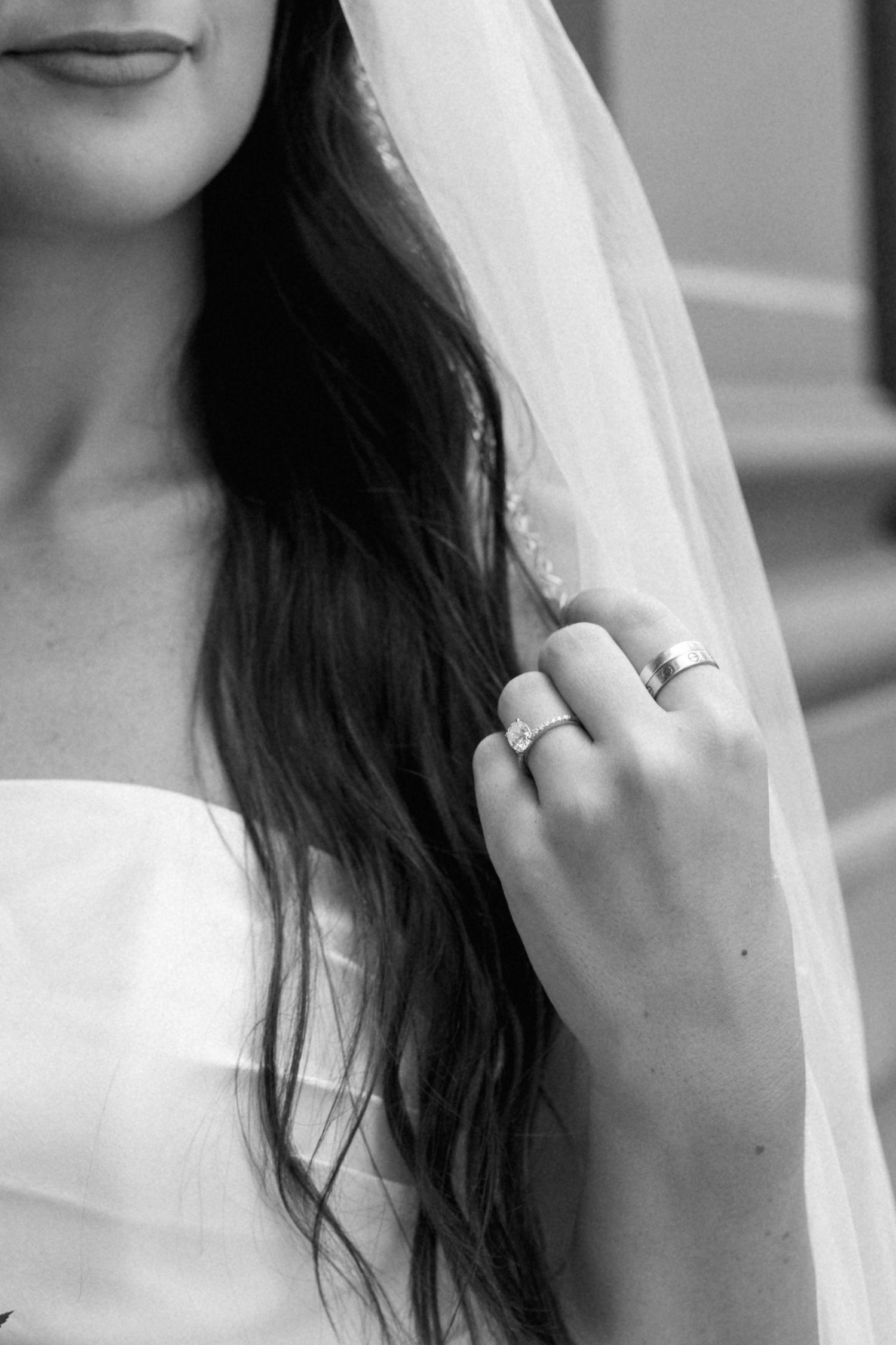 Black and white photo of a bride in a white gown and veil, showcasing her diamond engagement ring and wedding band.