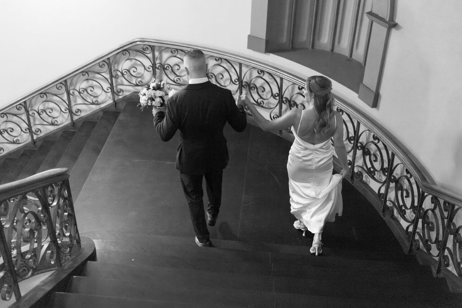 Person walks down ornate hallway with wrought iron railing while holding a white shopping bag.