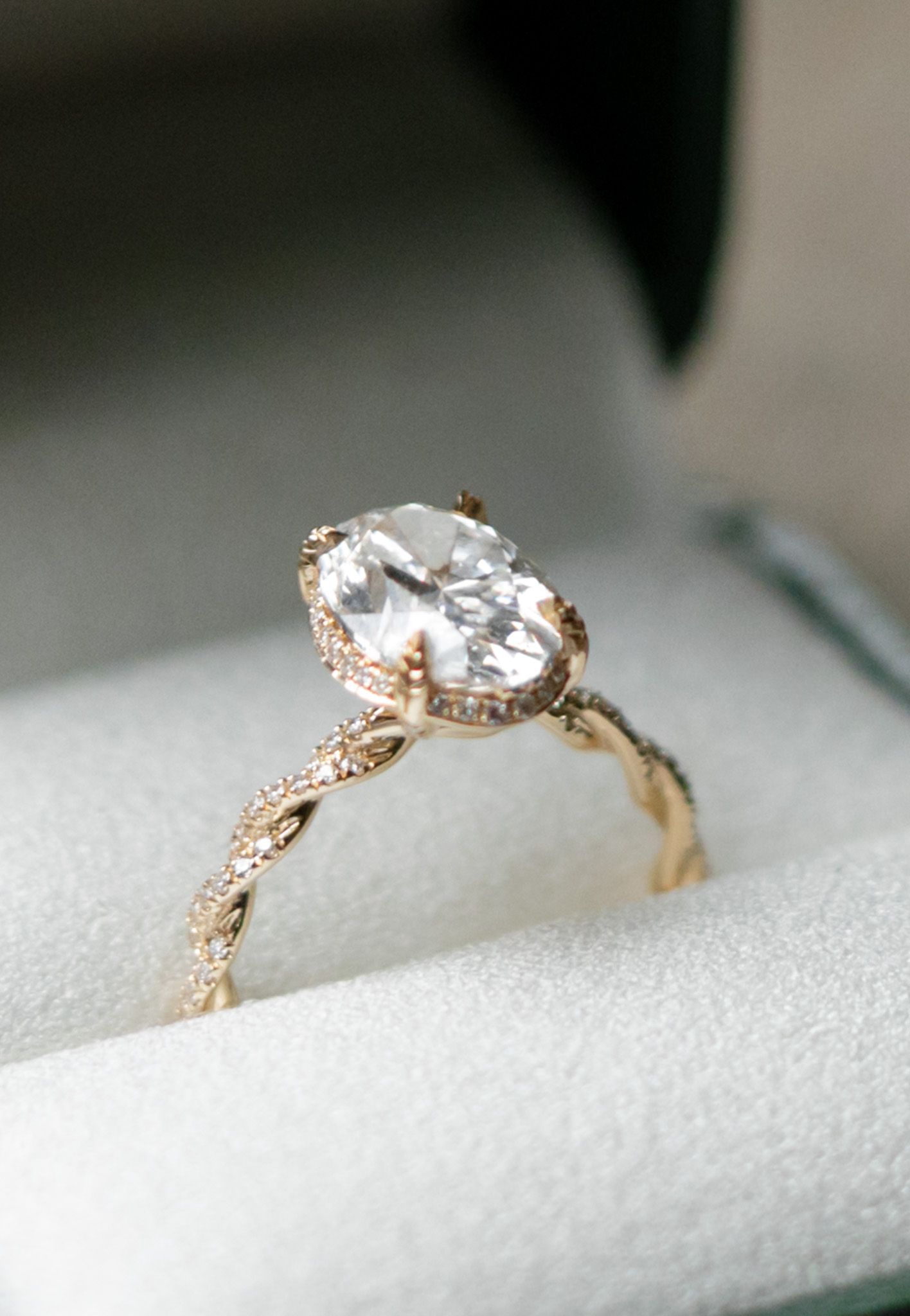 Elegant oval diamond engagement ring in gold with intricate vintage-inspired band detailing on white surface.