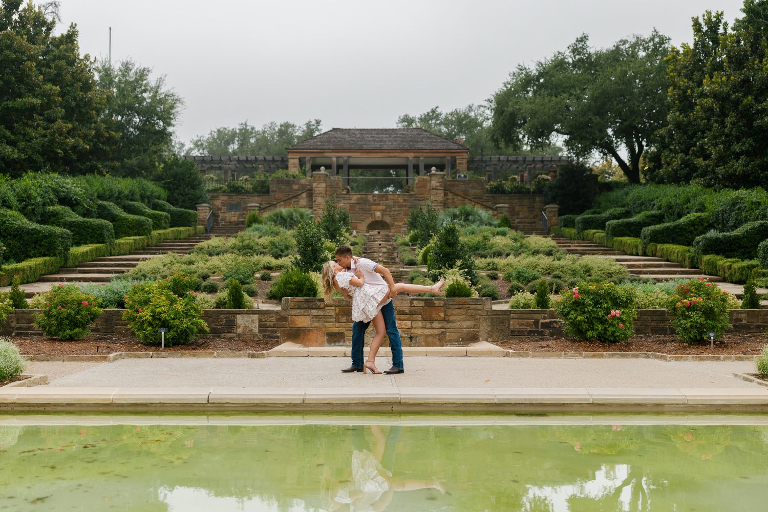 A couple shares a romantic moment in a formal garden with terraced landscaping and a reflecting pool at Fort Worth Botanic Garden.