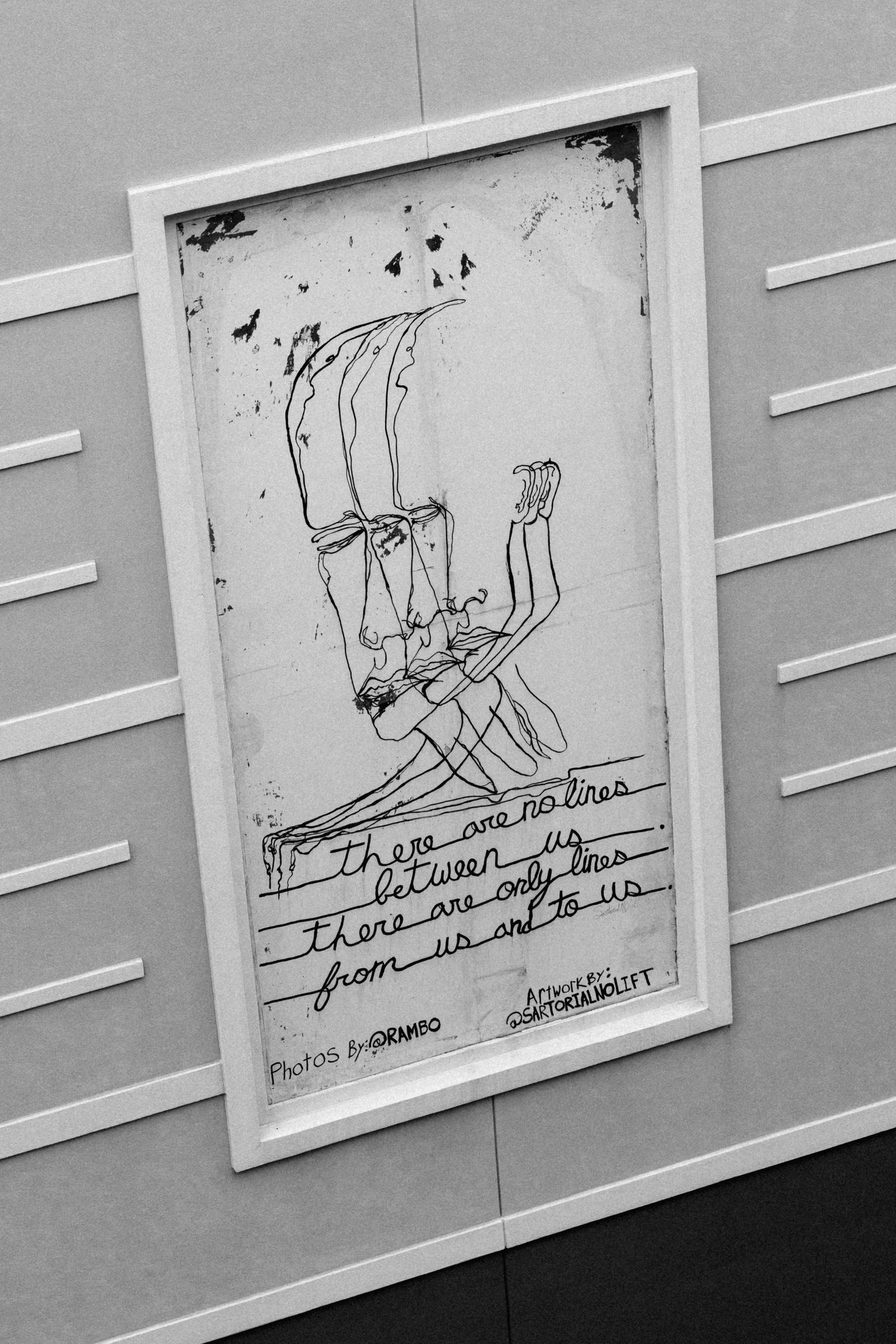 Black and white framed artwork with line drawing figures and handwritten text reading there are no lines between us.