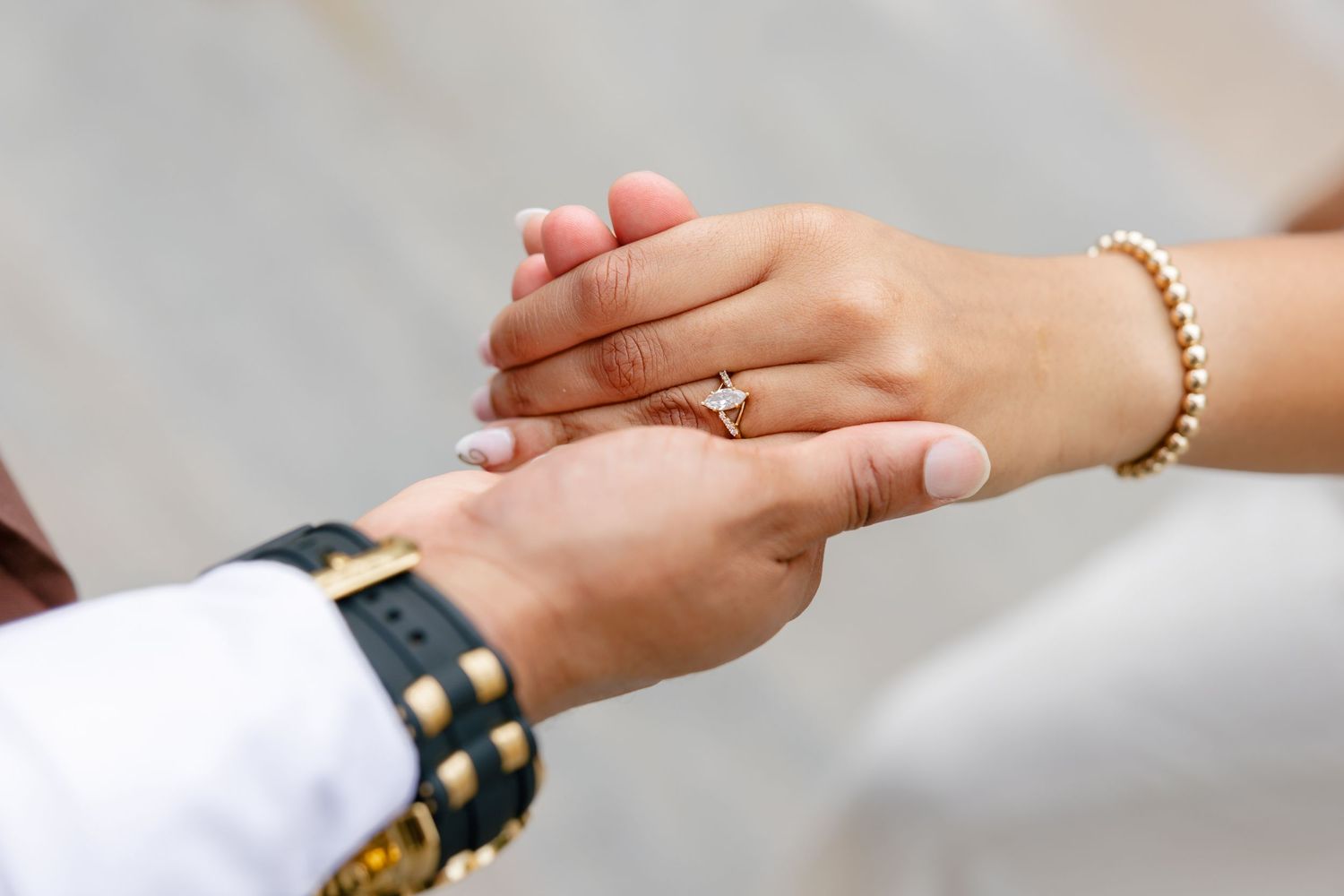 Close-up of hands exchanging rings during a wedding ceremony, with one person wearing a gold bracelet.
