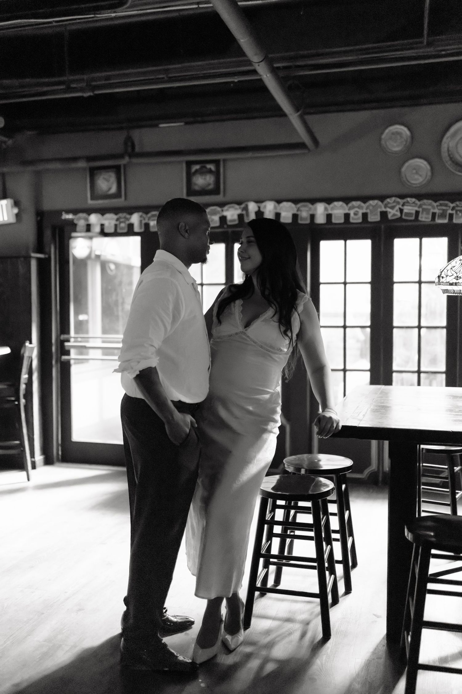 Black and white photo of a couple sharing an intimate moment in a rustic restaurant bar setting.
