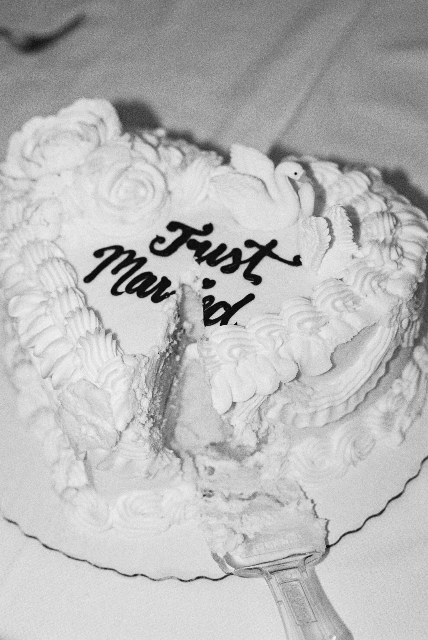 Black and white photo of a Just Married wedding cake being cut, decorated with white frosting roses and doves.