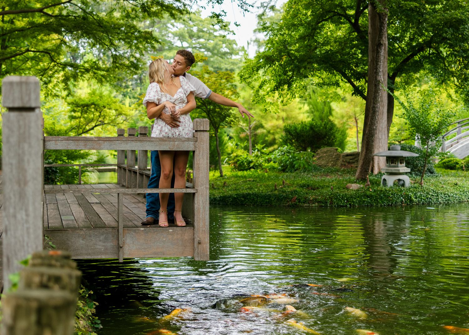 Couple enjoying a romantic moment together on a wooden dock by a serene lake surrounded by lush greenery.