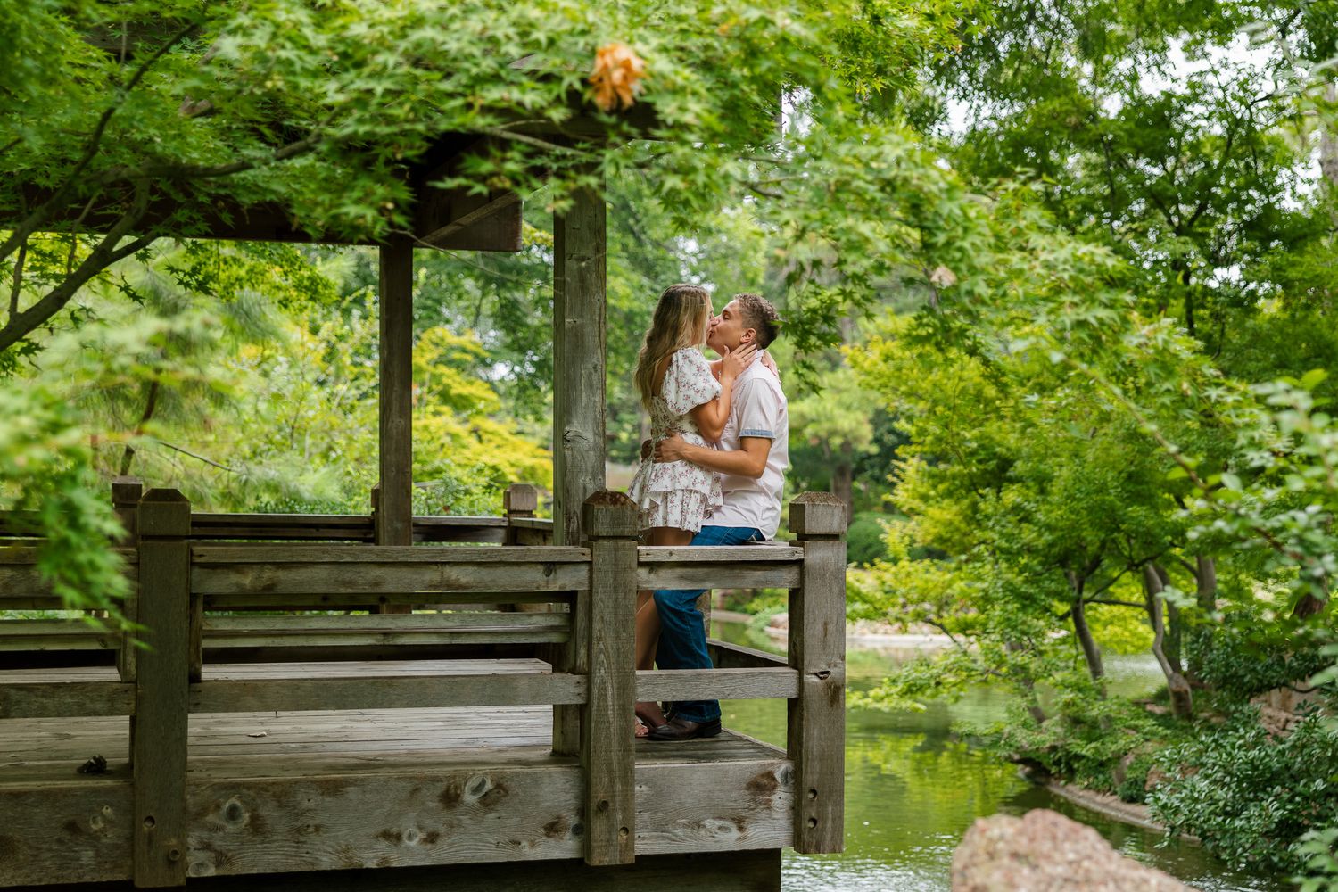Group relaxes on rustic wooden deck overlooking peaceful pond in wooded setting.