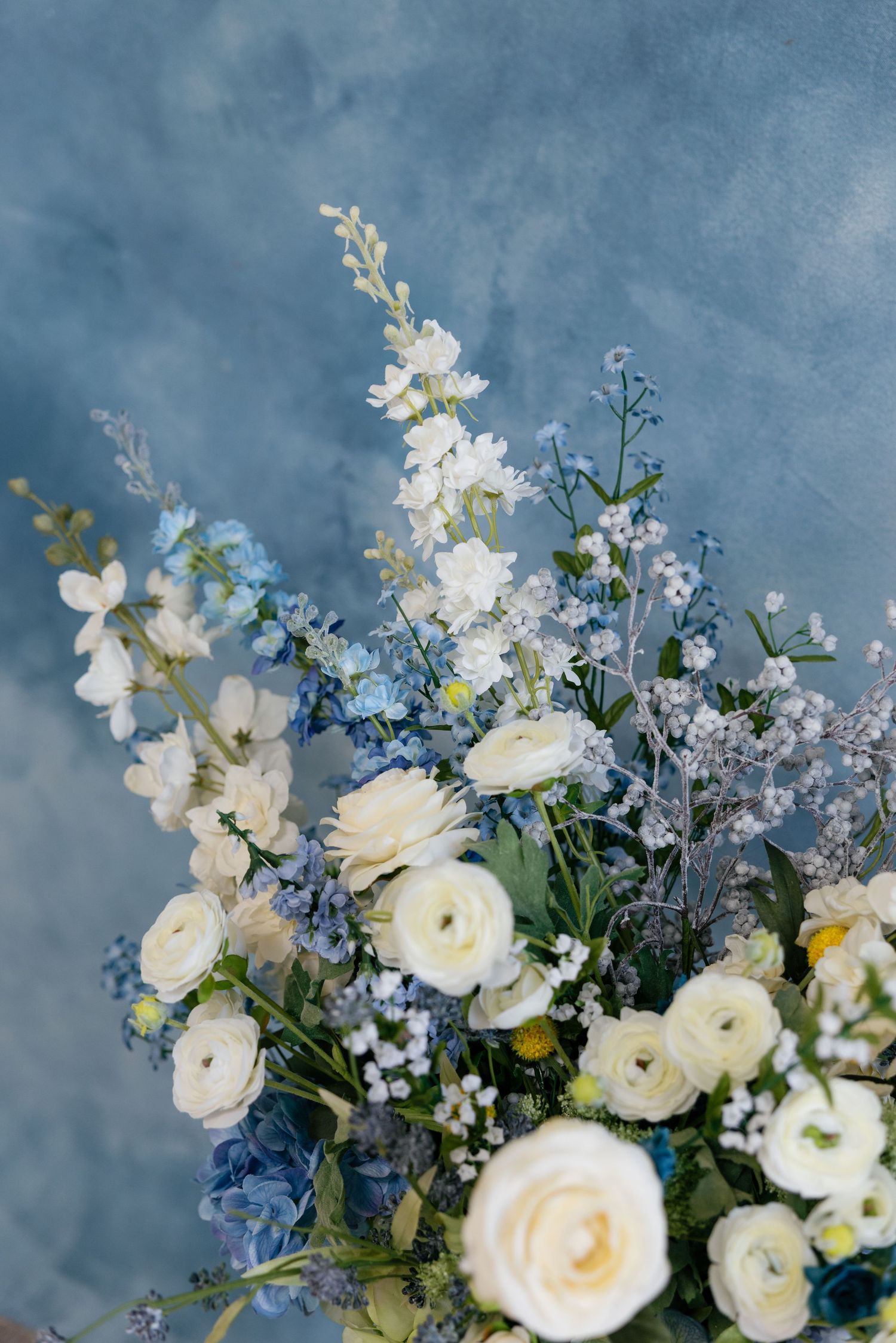 A romantic bouquet of white ranunculus and delphinium flowers arranged against a moody blue backdrop.