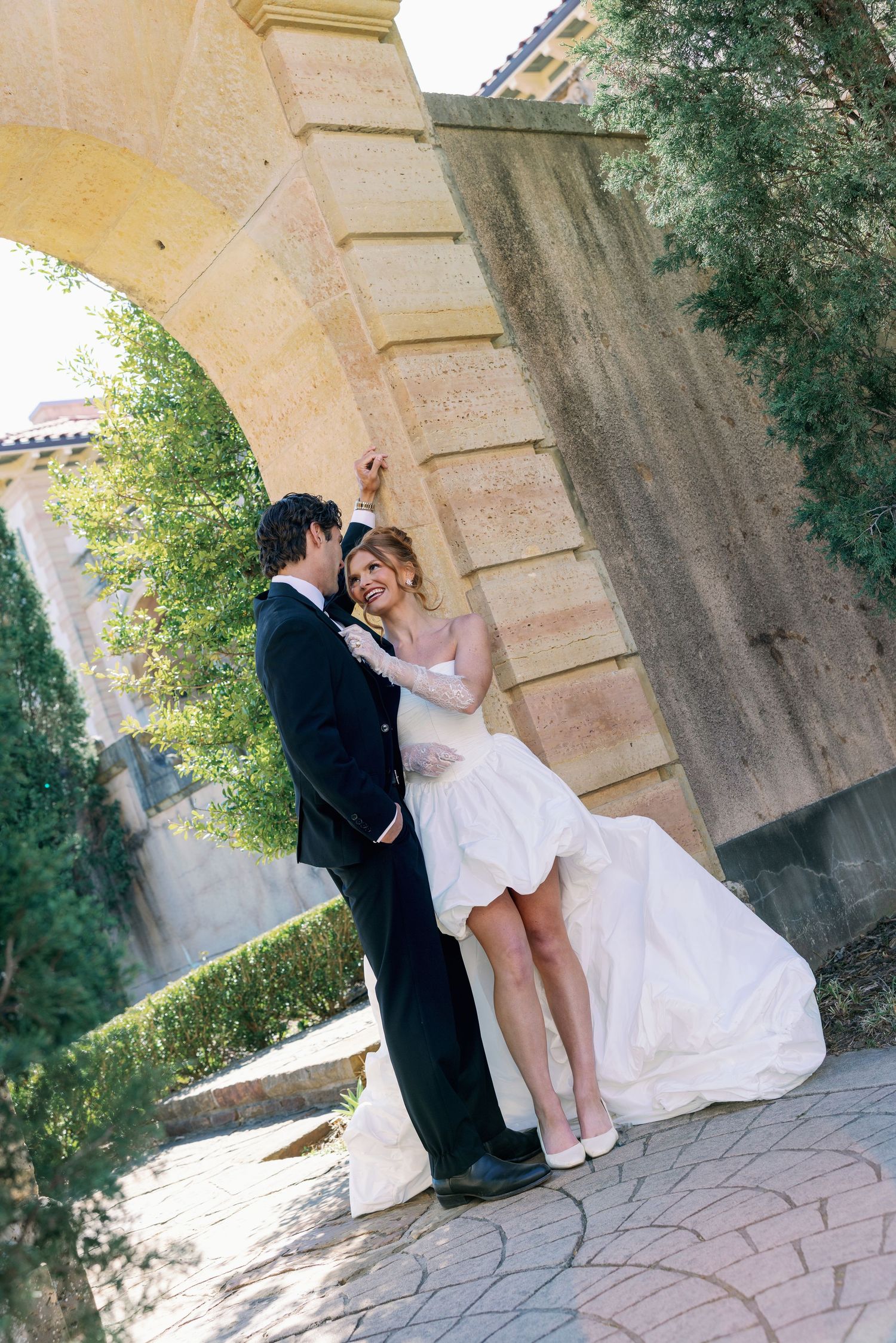 A bride and groom share a romantic moment under a stone arch surrounded by lush greenery on their wedding day.