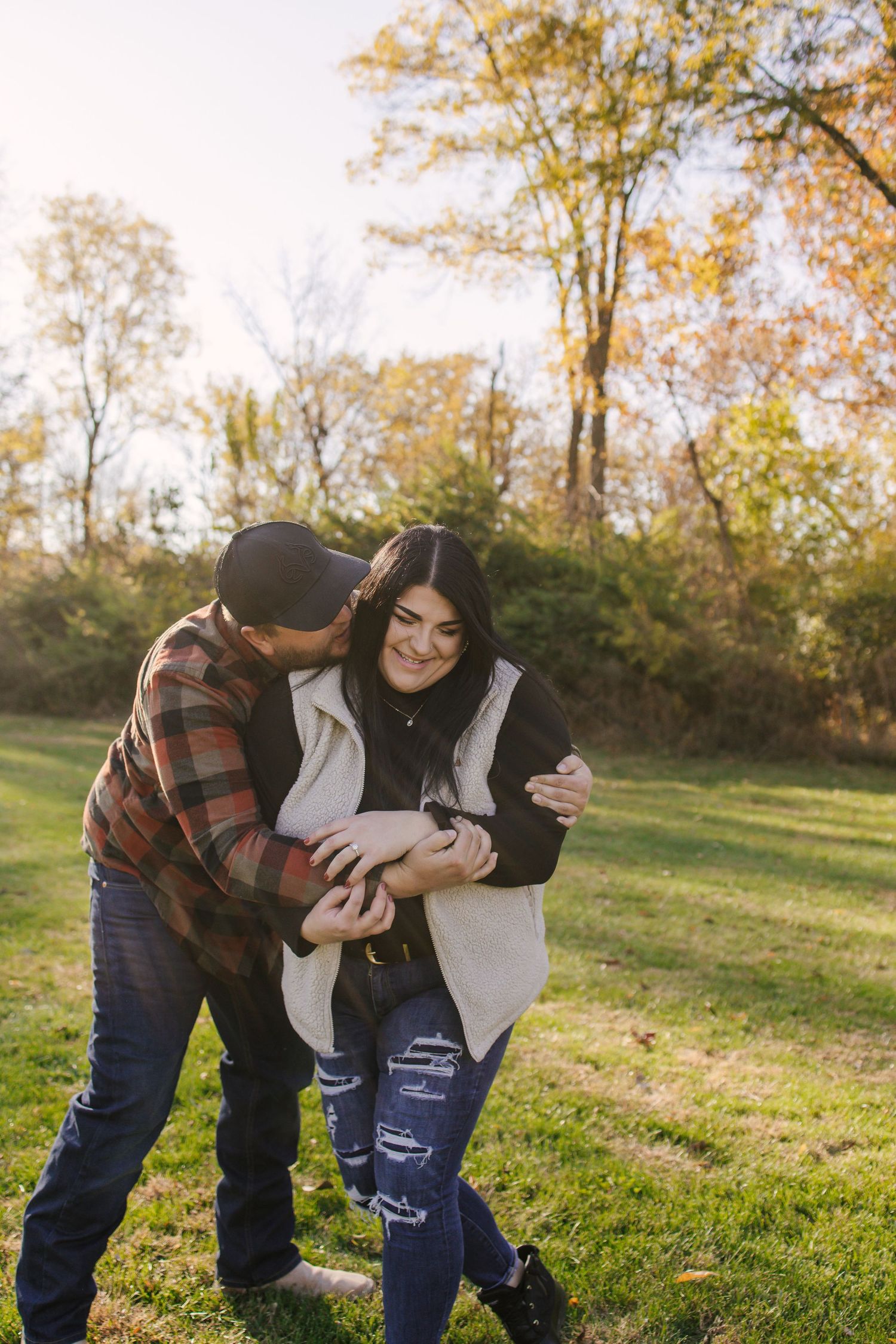 A couple shares playful moments together on a grassy hillside during a sunny autumn afternoon.