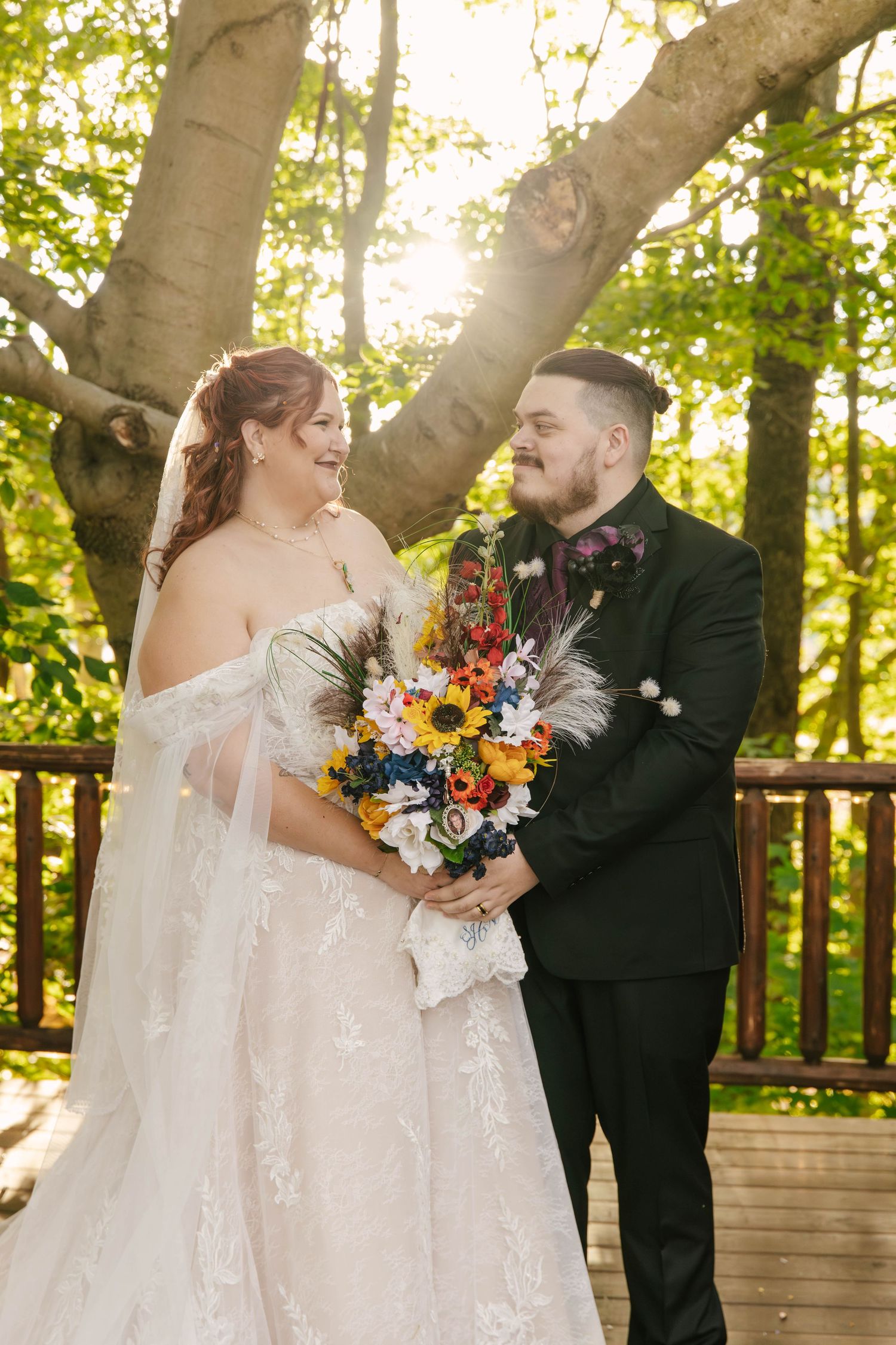A couple shares romantic moments on a wooden deck surrounded by lush green trees during their outdoor wedding ceremony.
