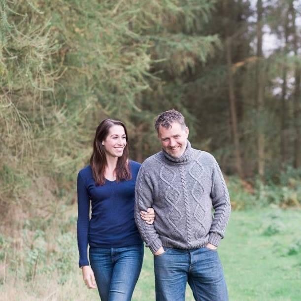Two people walking together on a path through a wooded area wearing casual clothing on an autumn day.