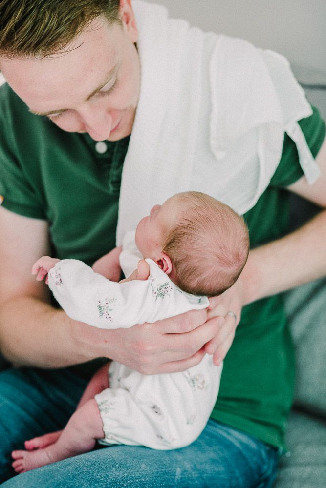 Tender moments captured of a newborn baby being cradled in white clothing.