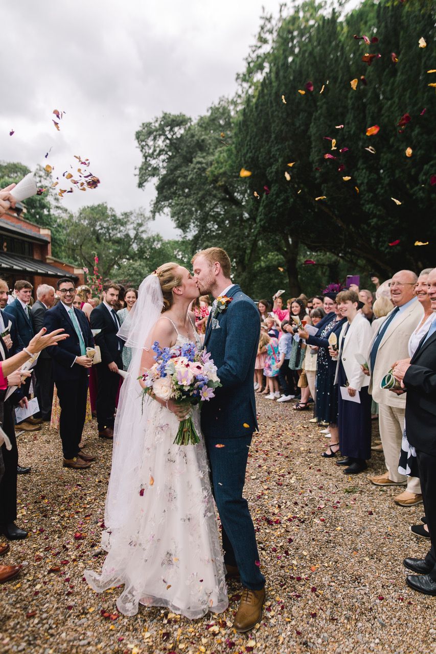 Wedding guests shower newlyweds with colorful flower petals during an outdoor forest ceremony celebration.