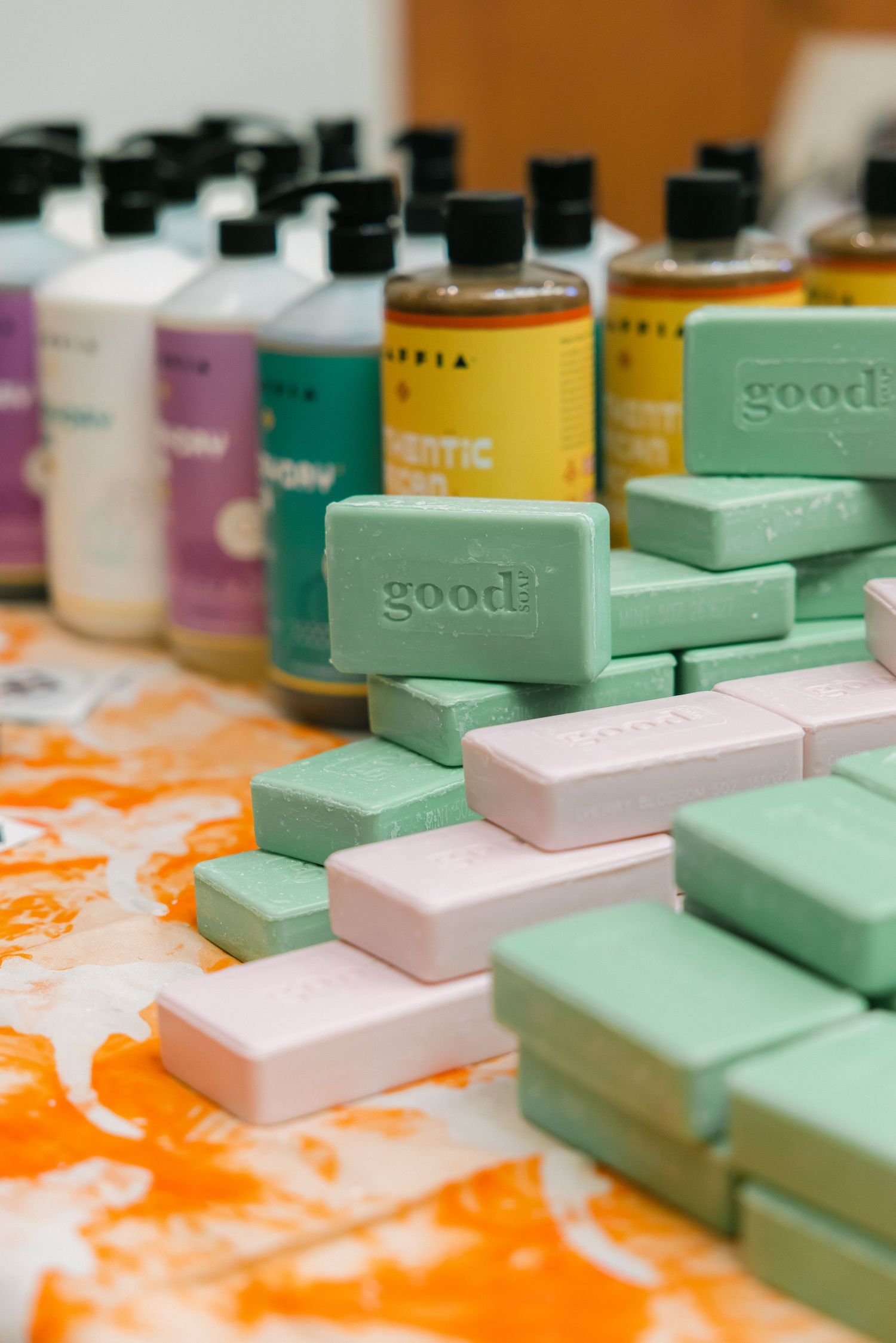 Assorted green and pink Good soap bars displayed on a colorful surface with bottles of liquid soap in the background.