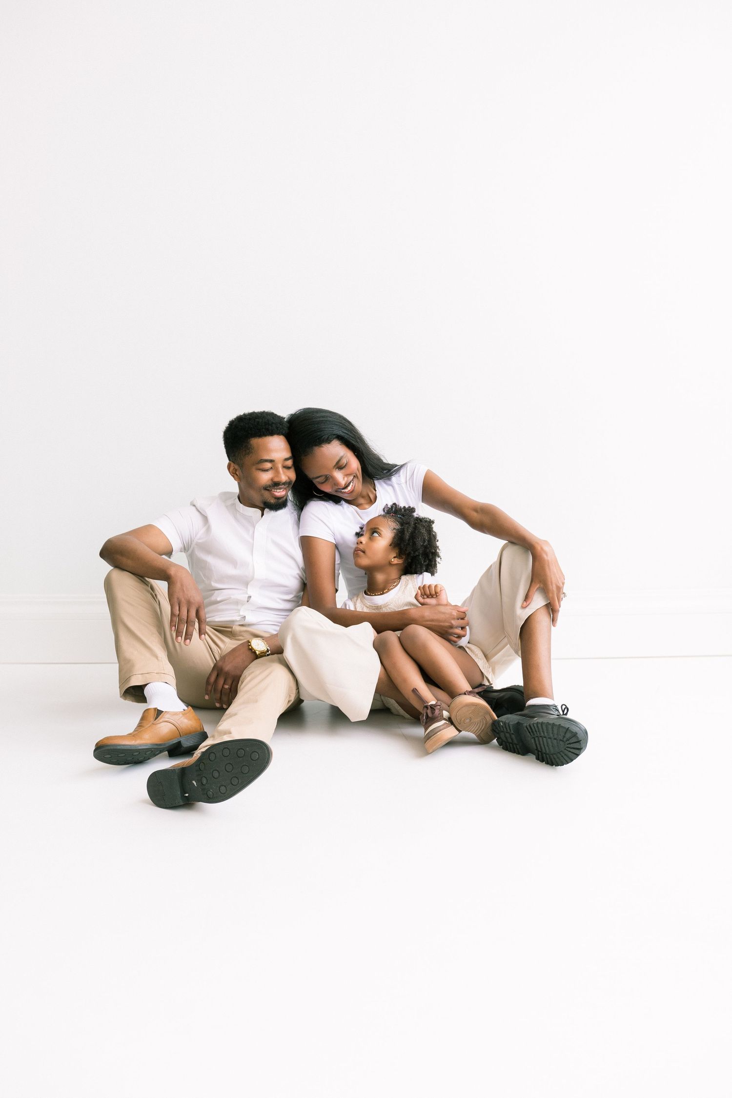 Happy African American family of three sitting together on white floor, parents embracing young daughter warmly.