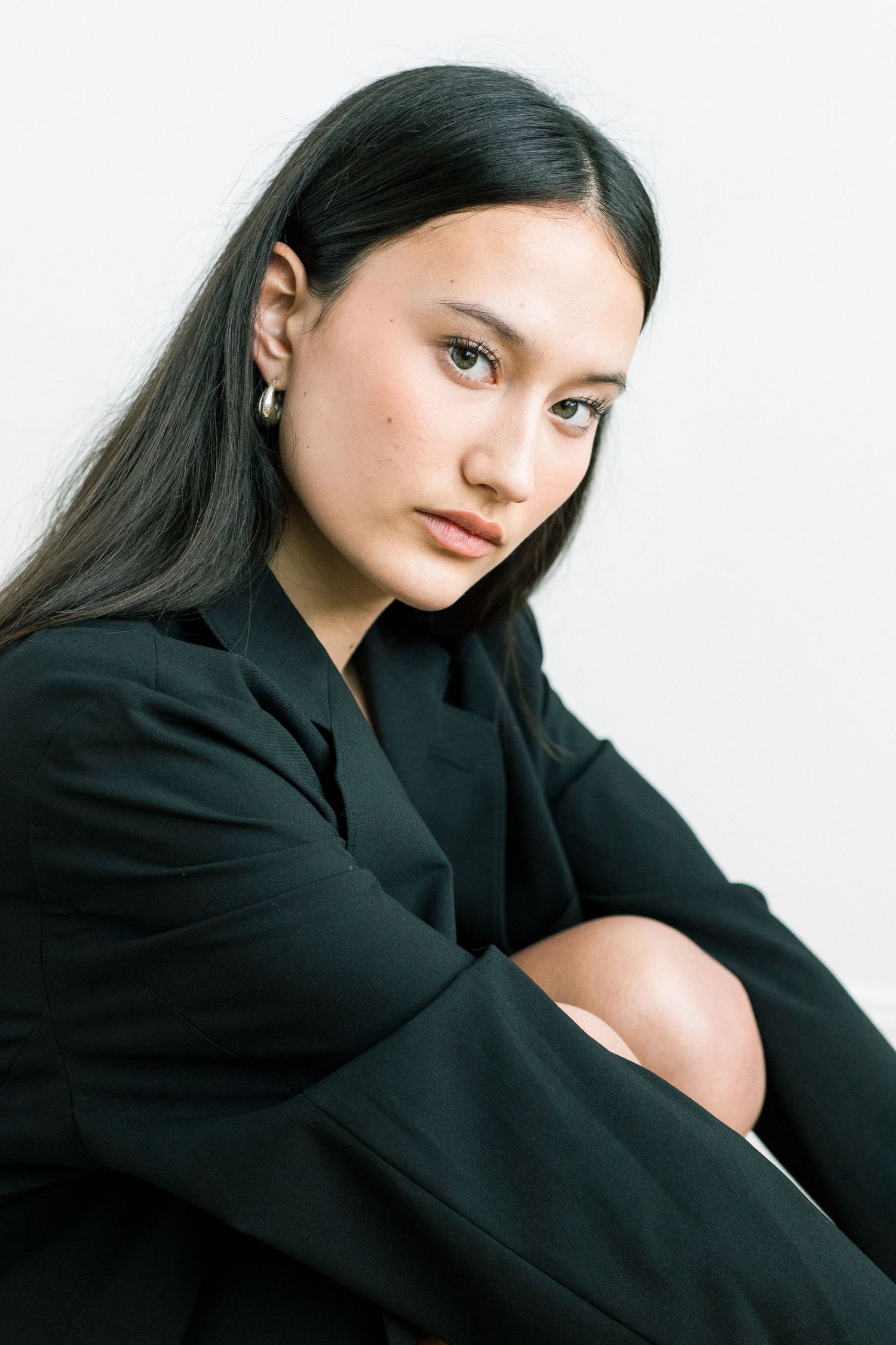 Young woman in black blazer sitting with knees up in minimalist black and white portrait.