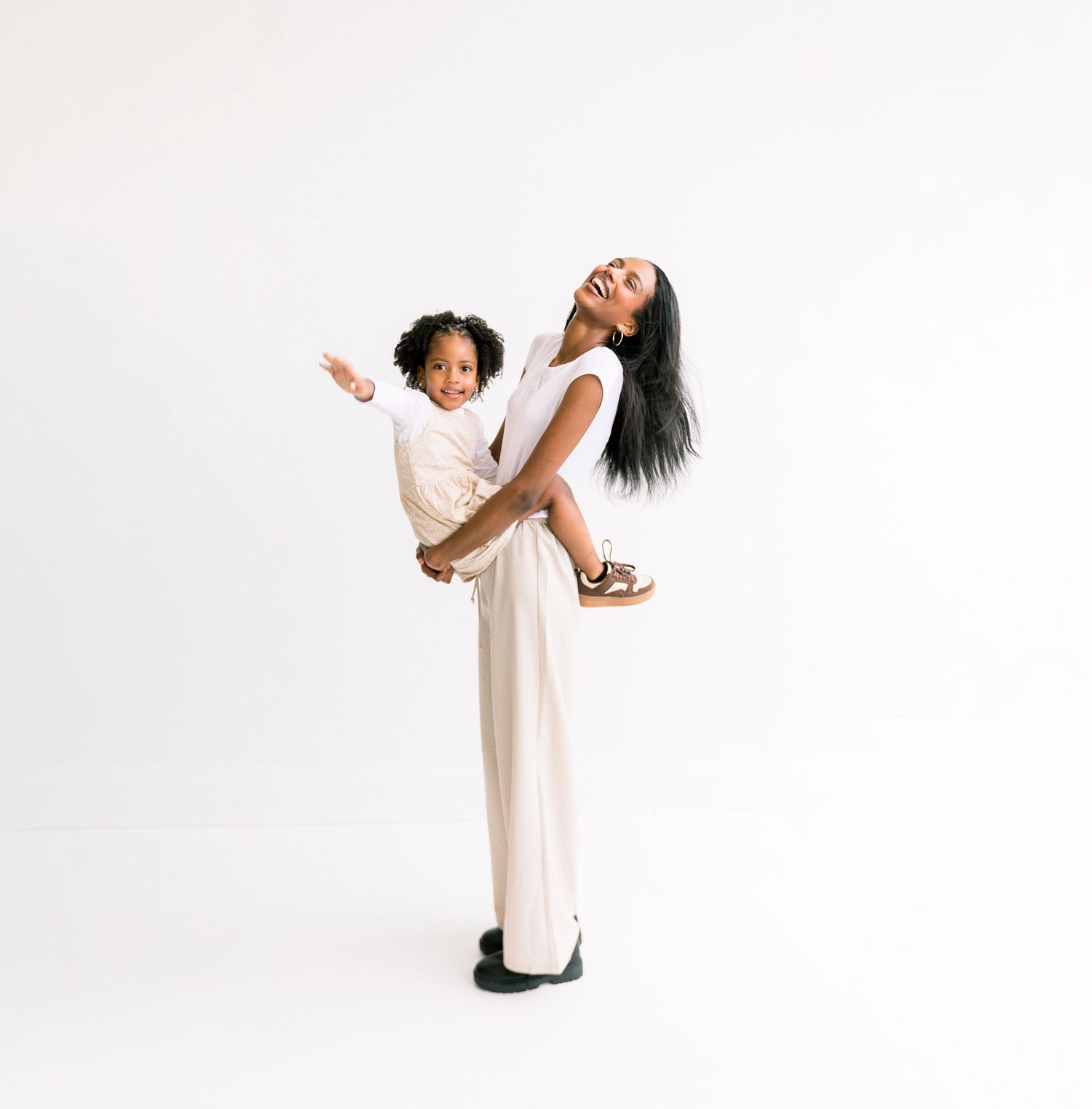 Joyful mother holding laughing child, white background studio portrait.