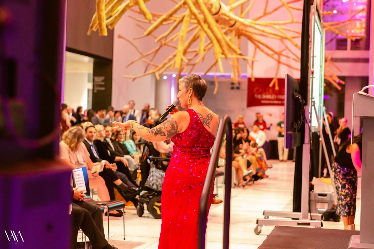 A woman in a red gown presents at an elegant indoor gala event.