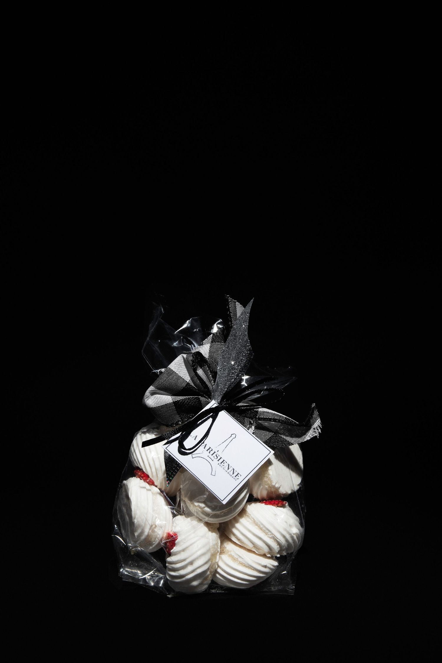 Elegant clear gift bag filled with white meringues, tied with a black ribbon bow and gift tag on black background.