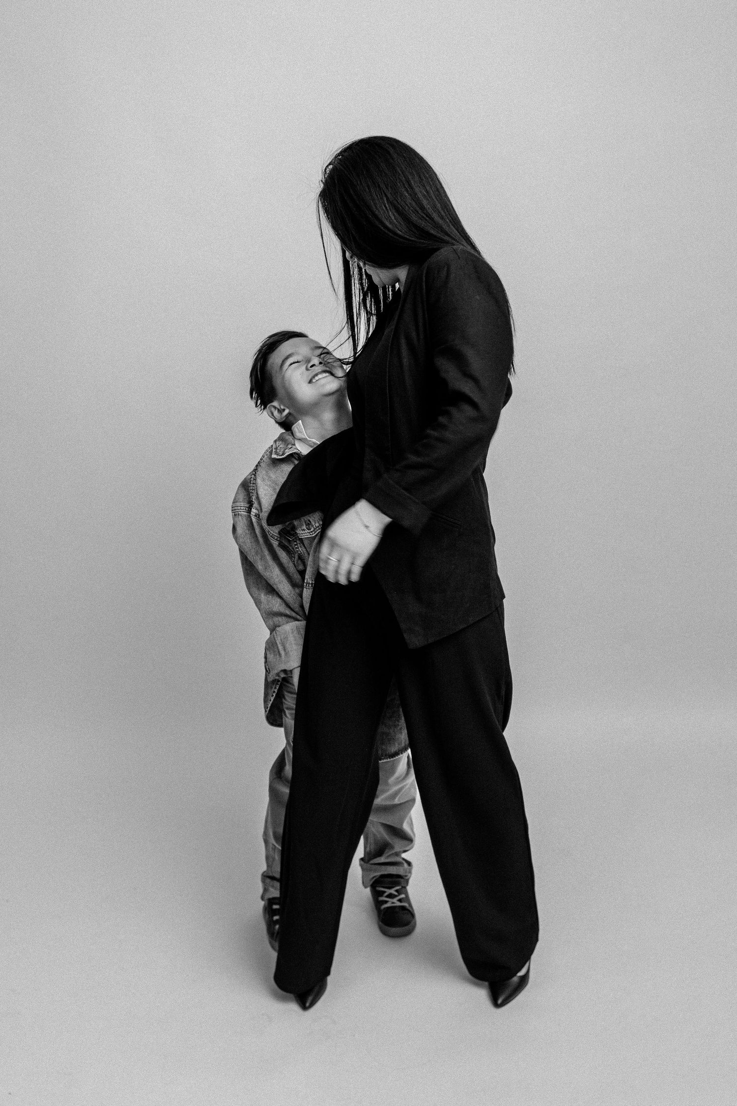 Black and white photo of two people embracing dramatically in a studio, one in a black suit, the other leaning back.
