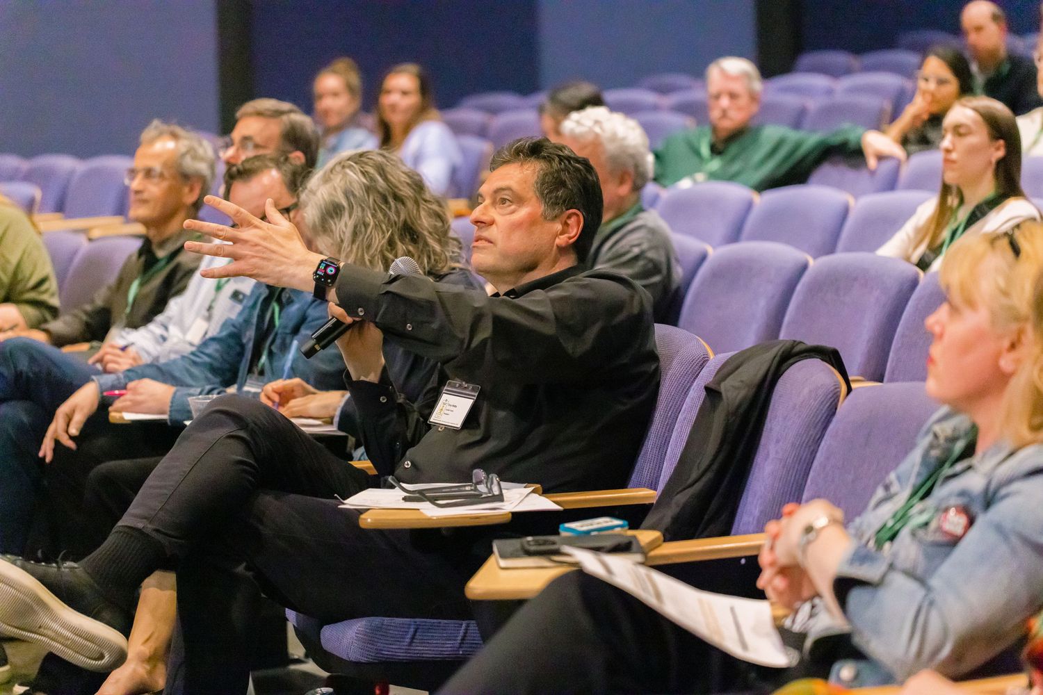 Audience members sitting in purple theater seats during an academic conference presentation.