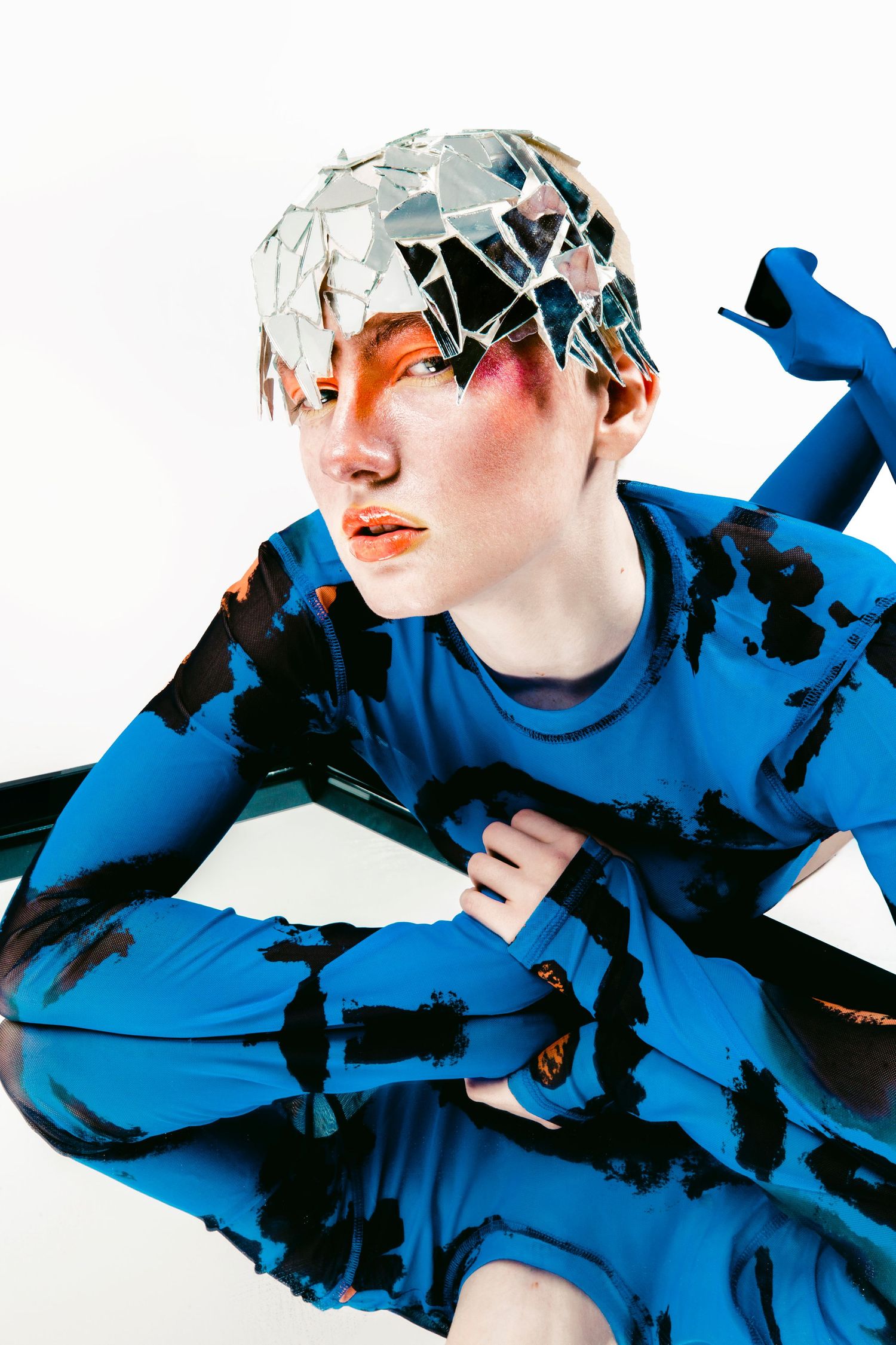 Editorial fashion portrait of a model in blue tie-dye outfit with shattered mirror pieces on head.