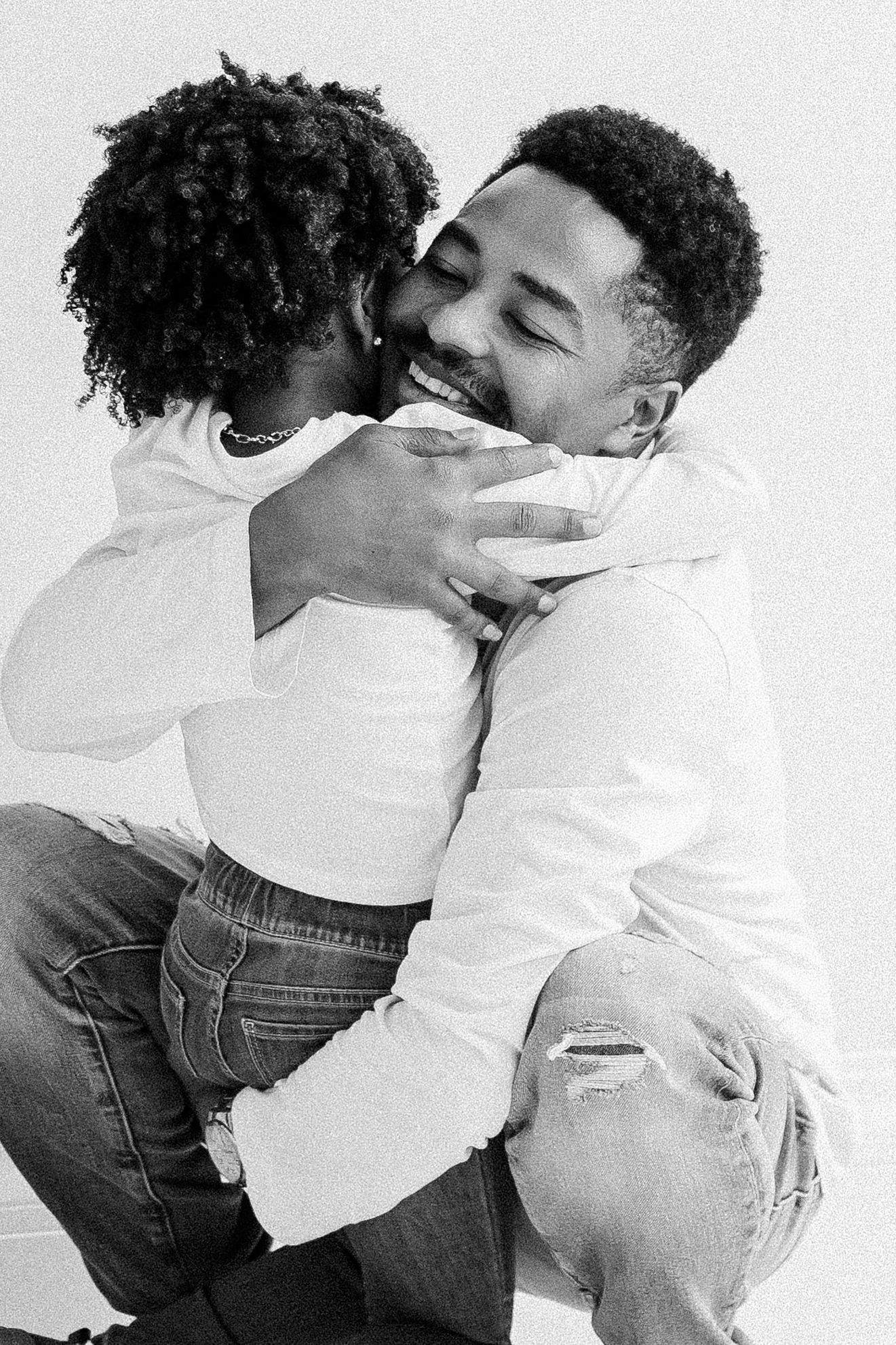 Black and white photo of two people sharing a warm embrace and kiss, both wearing white tops and jeans.