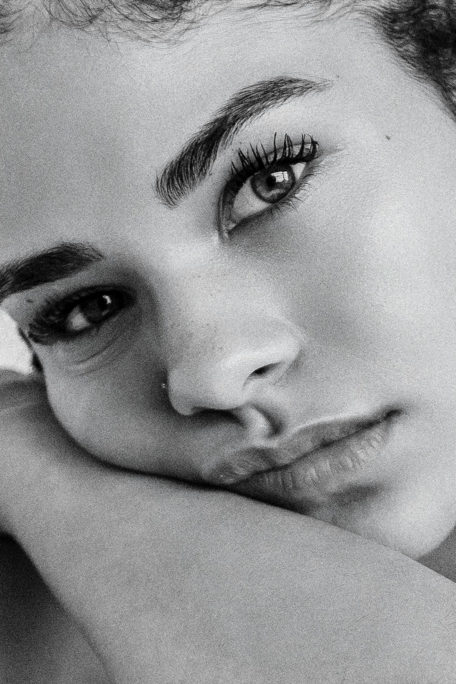 Black and white close-up portrait of a young woman resting her chin on her hands with striking eyes.