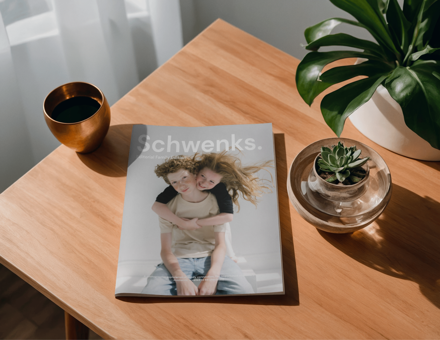 A personalized Schwenks photo magazine featuring two children lies on a wooden table beside a coffee cup and succulent plant.
