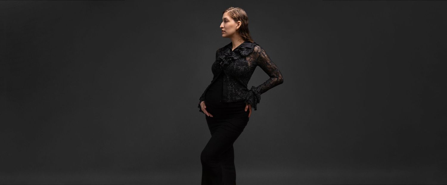 Elegant woman in black lace top and wide-leg trousers posing against dark gray background.