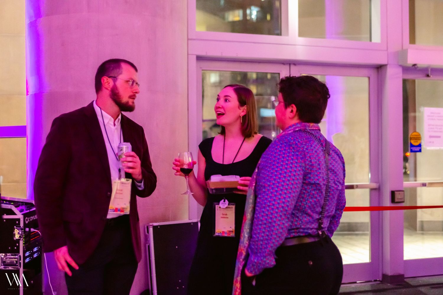 Three professionals networking at evening conference event under purple ambient lighting.