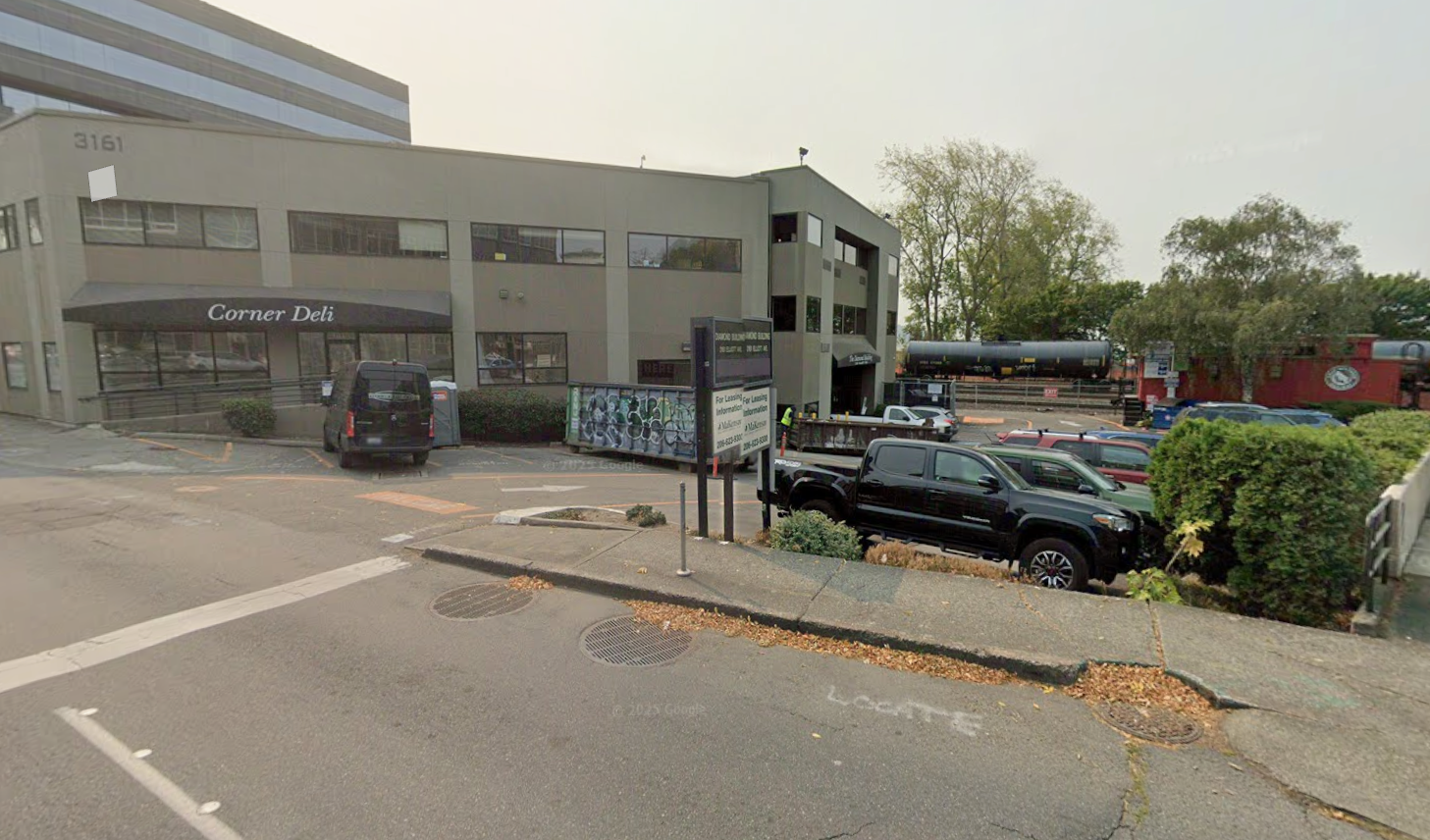 Corner Deli storefront with parking lot, black SUV, and multi-story office building in an urban commercial area.