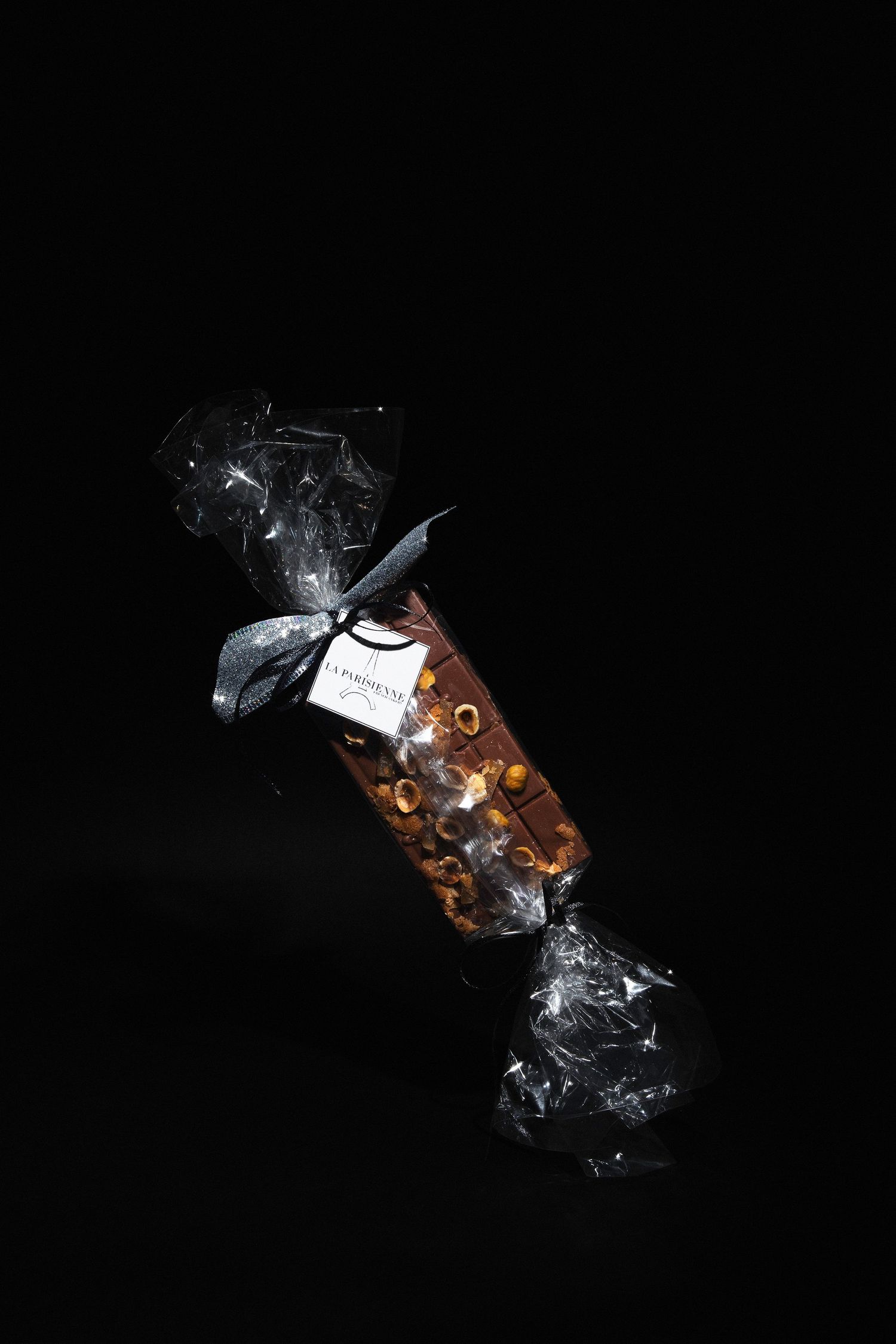 Chocolate bar with nuts wrapped in clear cellophane tied with a silver bow on a black background.