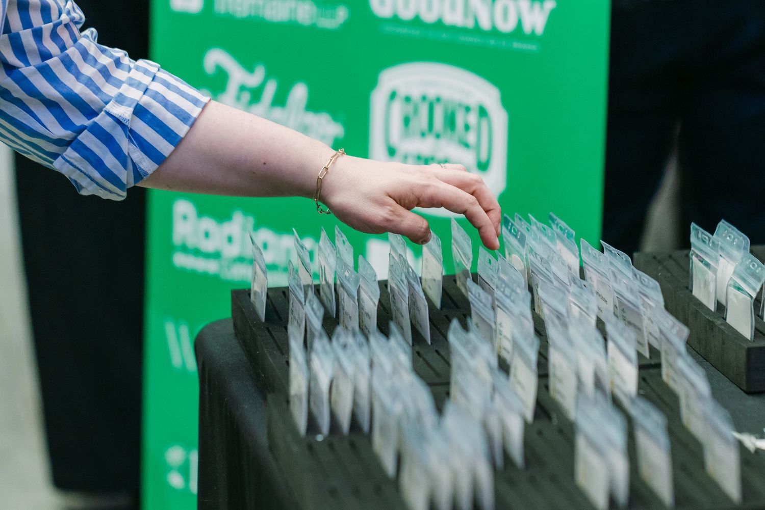 Hand reaching for name tags at a Crooked Media and RadioNow event registration table with green branded backdrop.